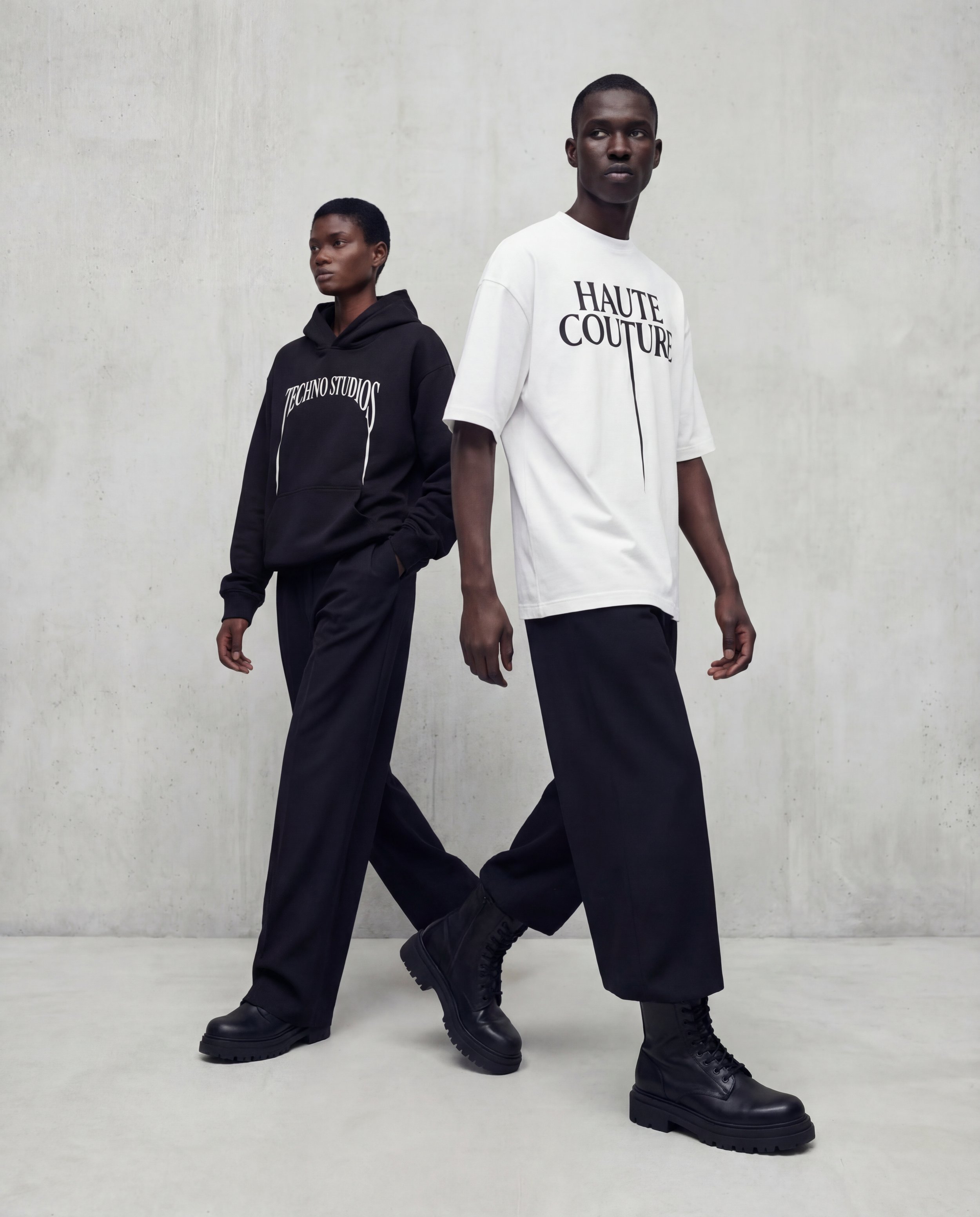 Models wearing Techno Studios oversized unisex apparel, including a white graphic t-shirt and black hoodie crafted from premium 100% cotton and made in Portugal. Designed with structured silhouettes and relaxed proportions, the garments reflect avant