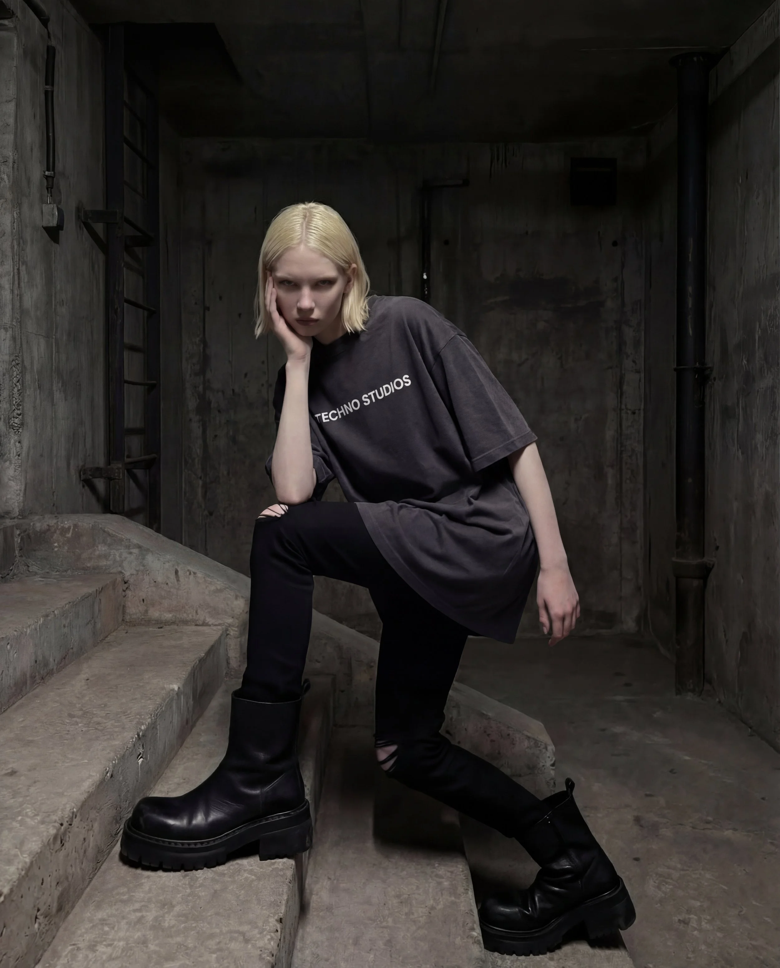 Model wearing the Techno Studios oversized dark t-shirt crafted from premium 100% heavyweight cotton and made in Portugal. The unisex relaxed silhouette features a structured fit with dropped shoulders, combining minimal branding with avant-garde ind