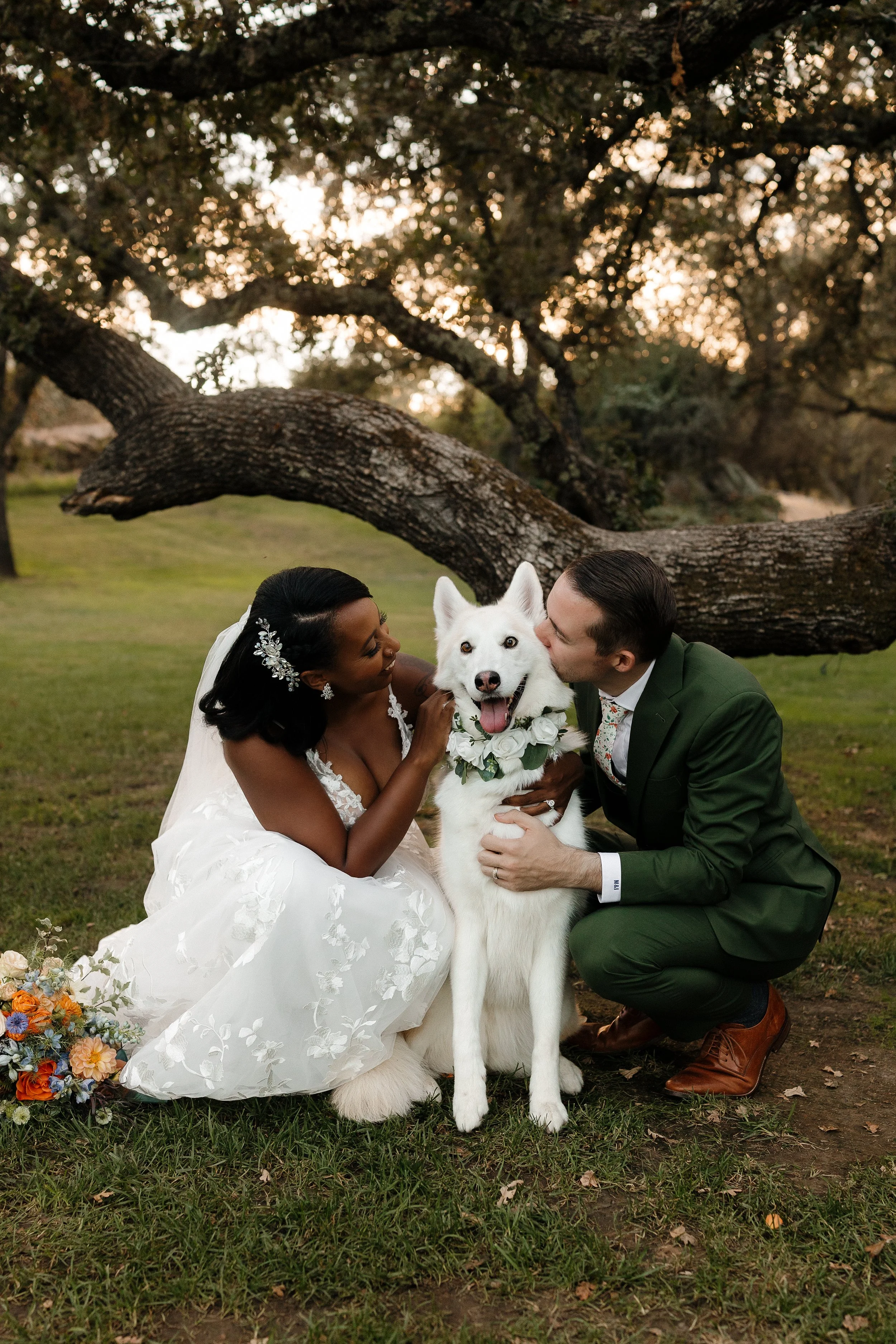 A white Husky mix smiling and posing with a bride and groom at Gold Hill Gardens in Newcastle, CA