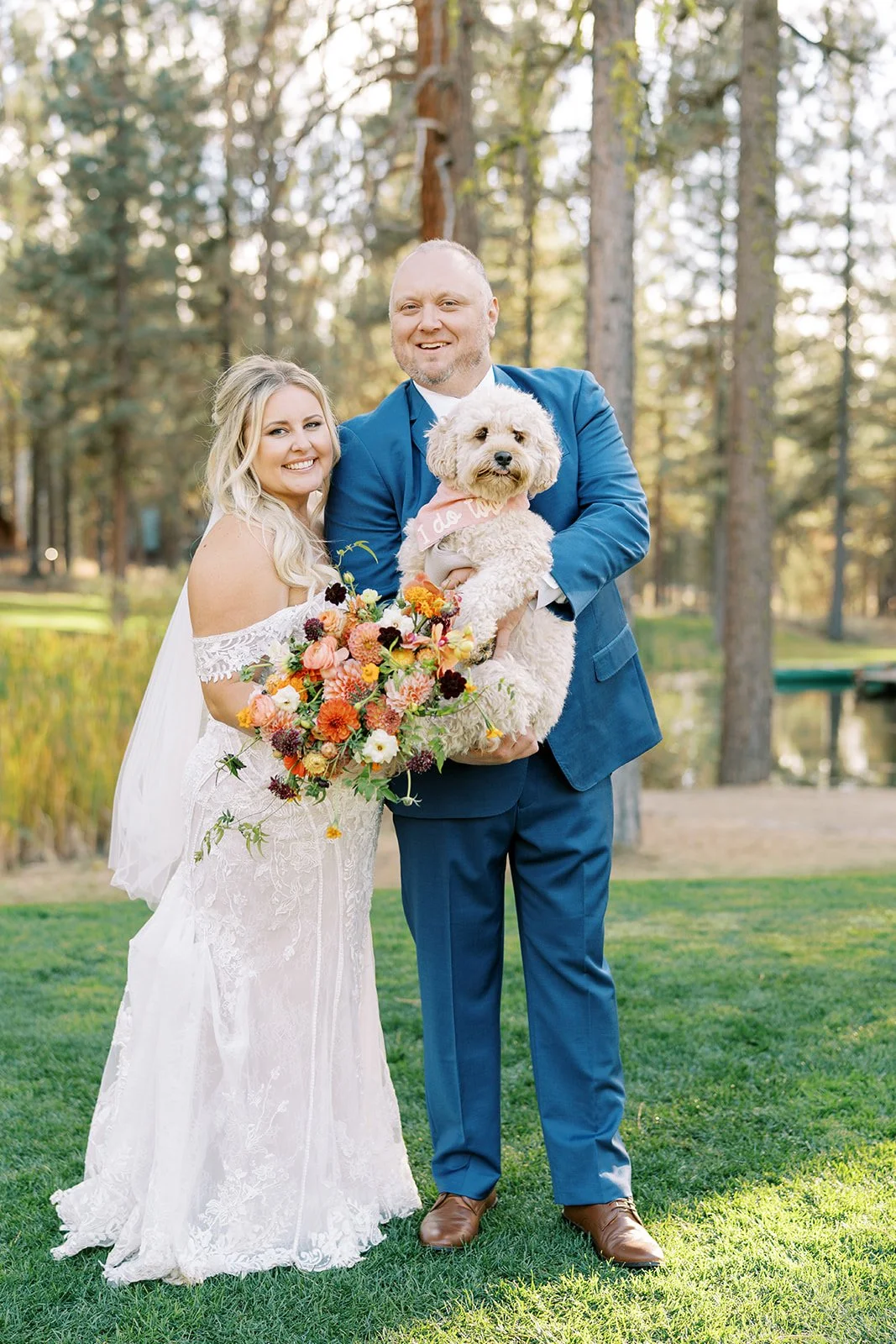 Doodle wearing an I Do too bandana being held by a bride and groom at Chalet View Lodge