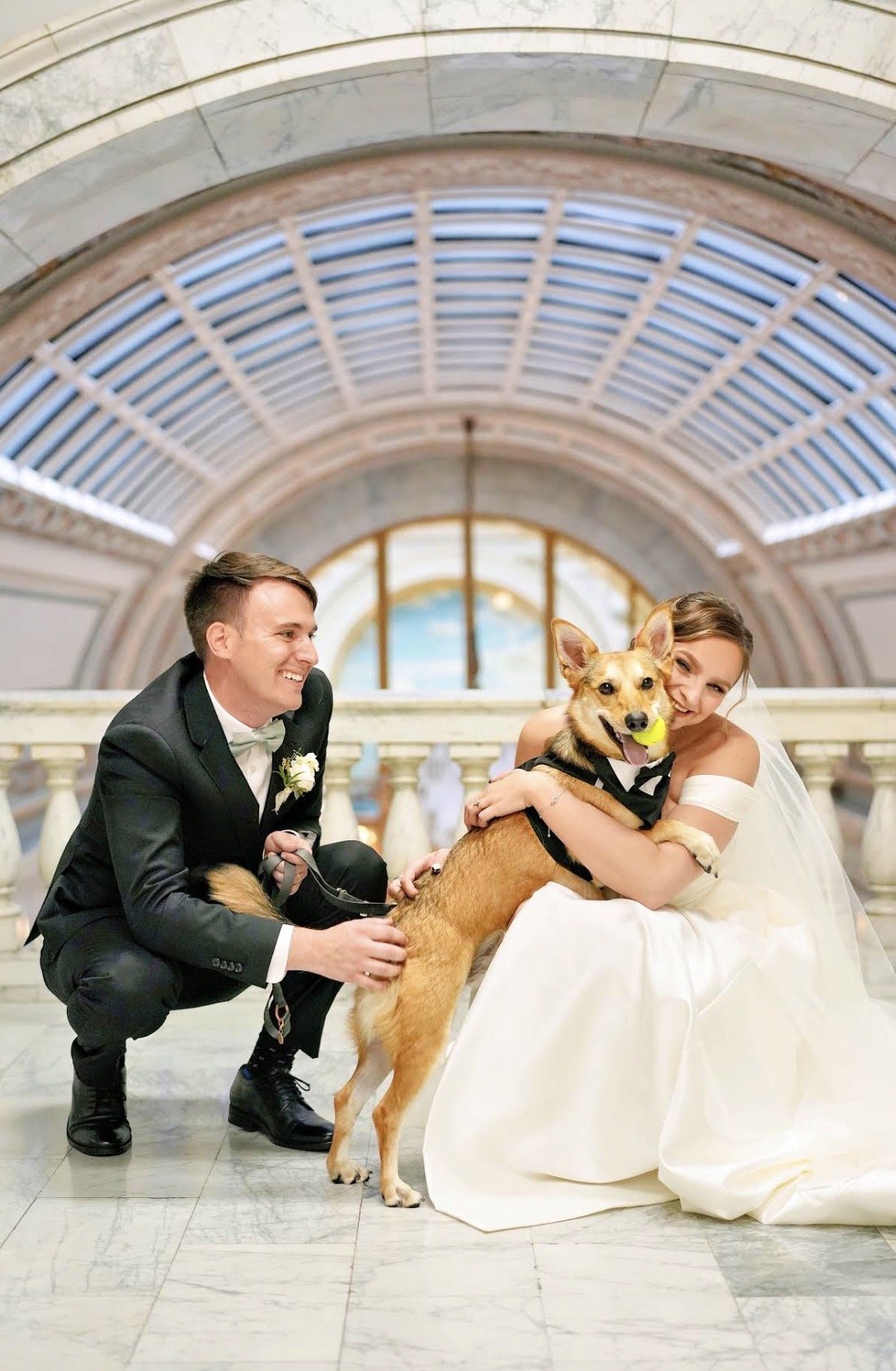 A wedding scene with a kneeling down with their dog in a tuxedo