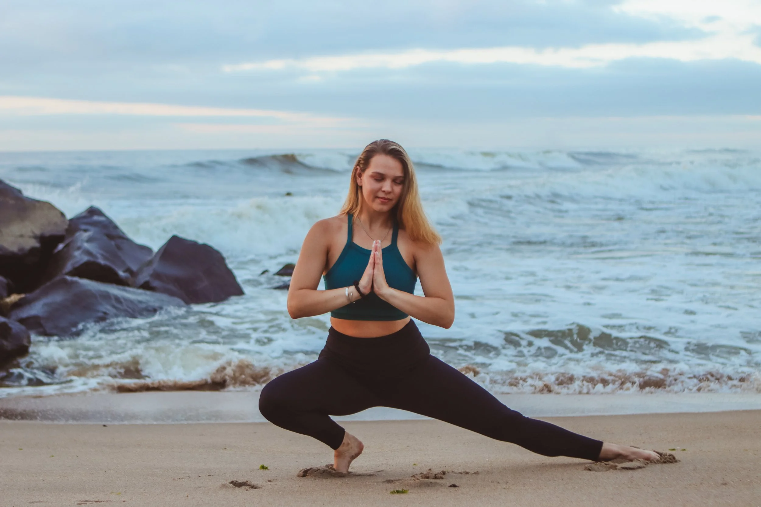 Woman practicing yoga on the beach with ocean in the background.