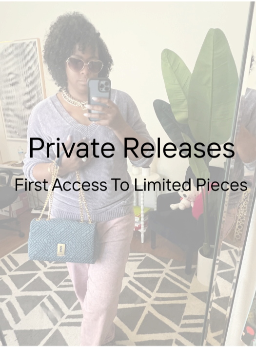 A woman taking a mirror selfie indoors. She is wearing sunglasses, a gray sweater, and pink pants, accessorized with a gold chain and a blue handbag. There is large green plant and a black sofa with plush toys in the background.