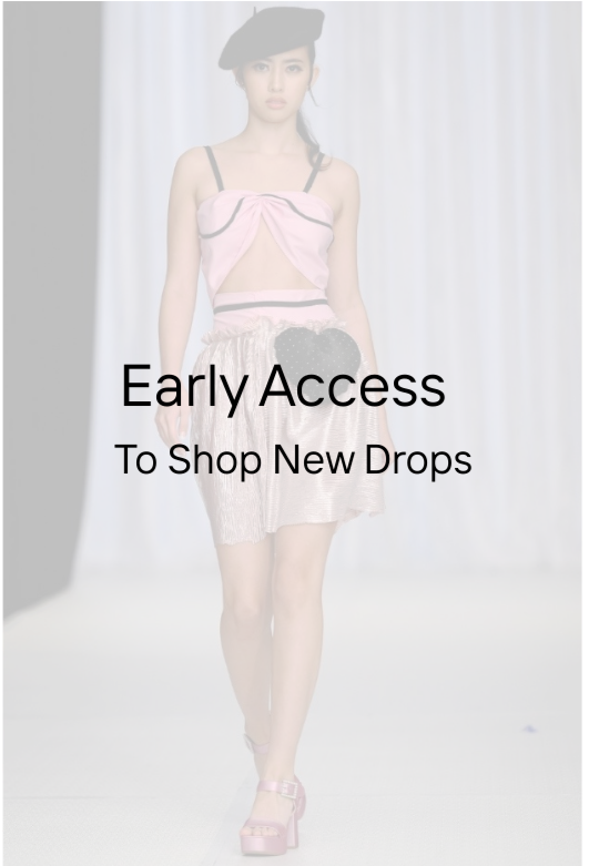 A young woman walking down a runway during a fashion show, wearing a pink and black top, a pink skirt, and pink high heels, with a black beret and a large black bow on her waist.