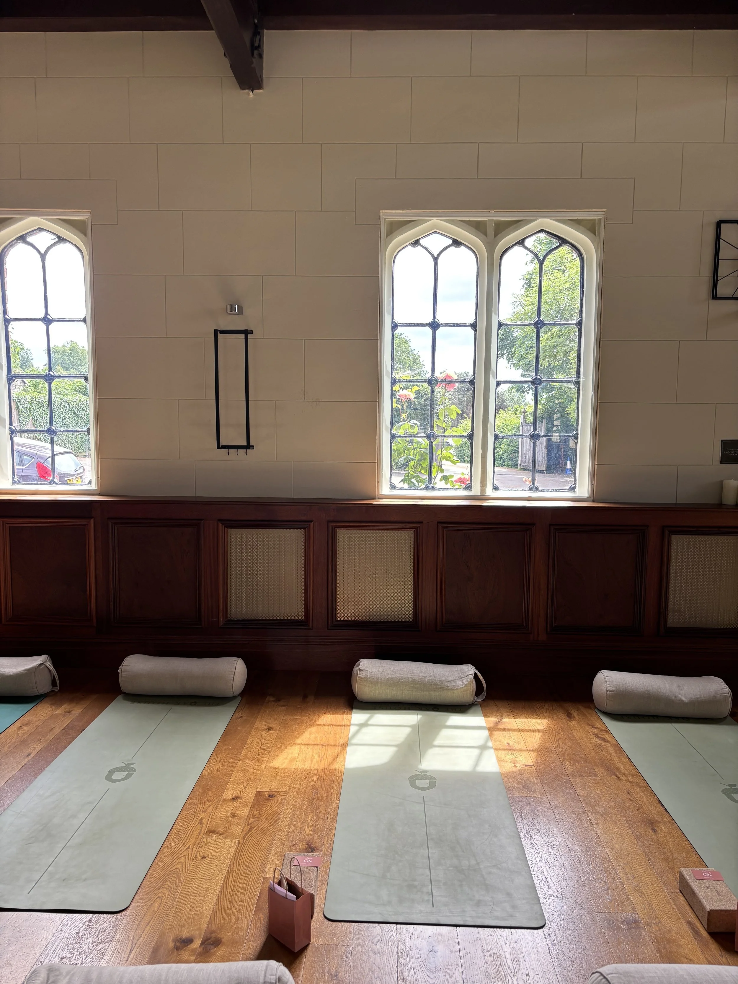 A woman sitting cross-legged on a yoga mat in a room with minimal decor, smiling.