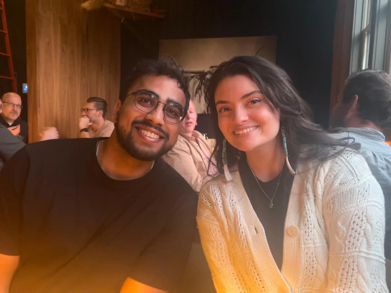 Two people smiling and sitting together in a restaurant, with other diners in the background.