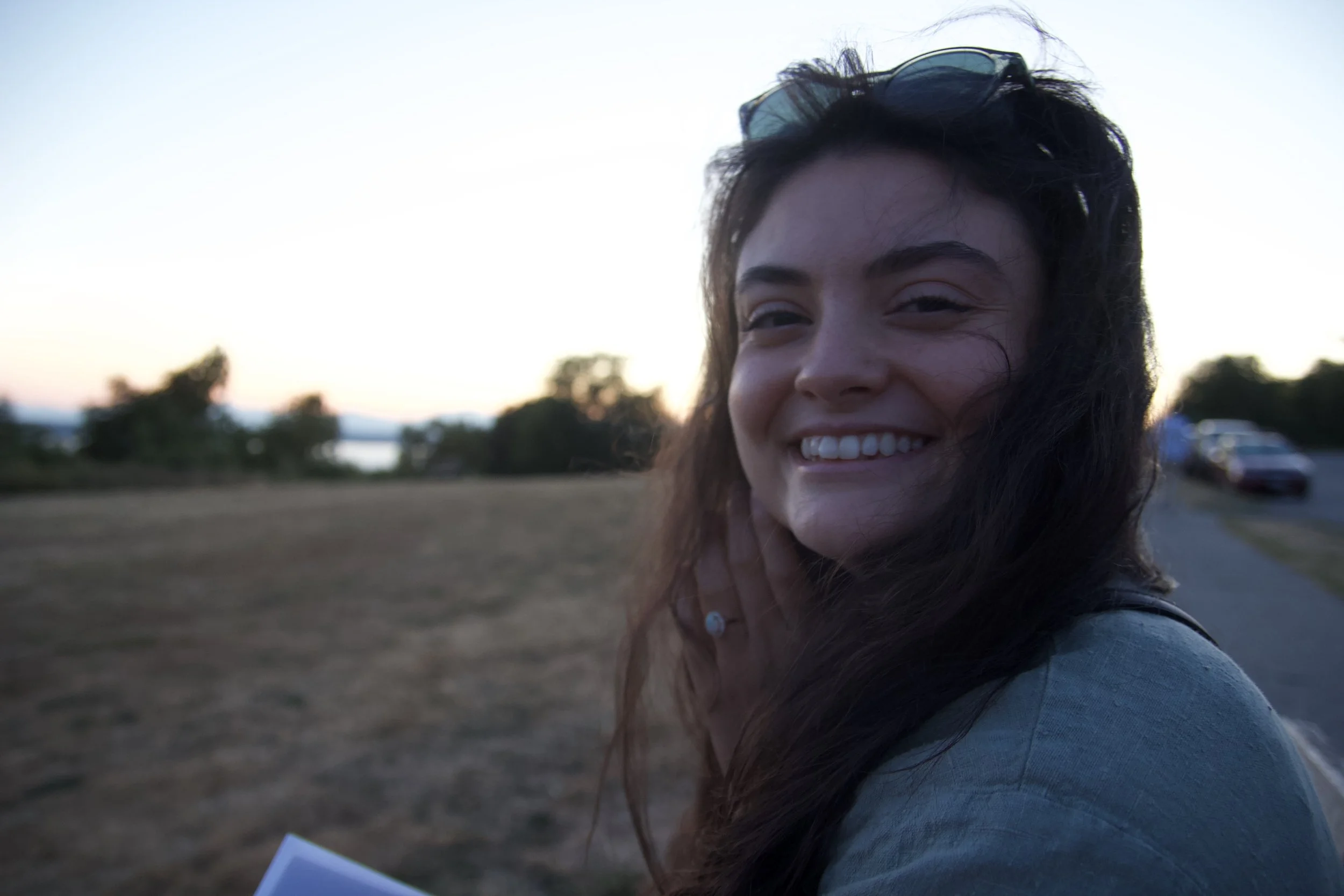 Ayșenur Ezgi Eygi  smiling outdoors at sunset, with trees and a parked car in the background.