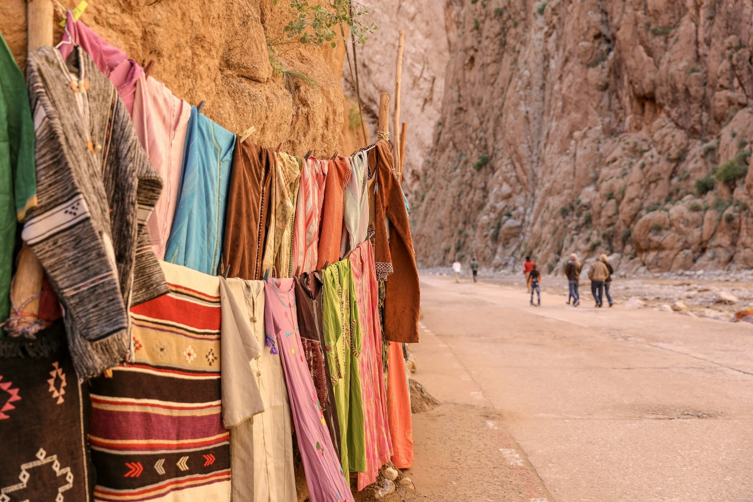 Colorful clothing hanging on a line against a rocky desert cliff with people walking in the distance.