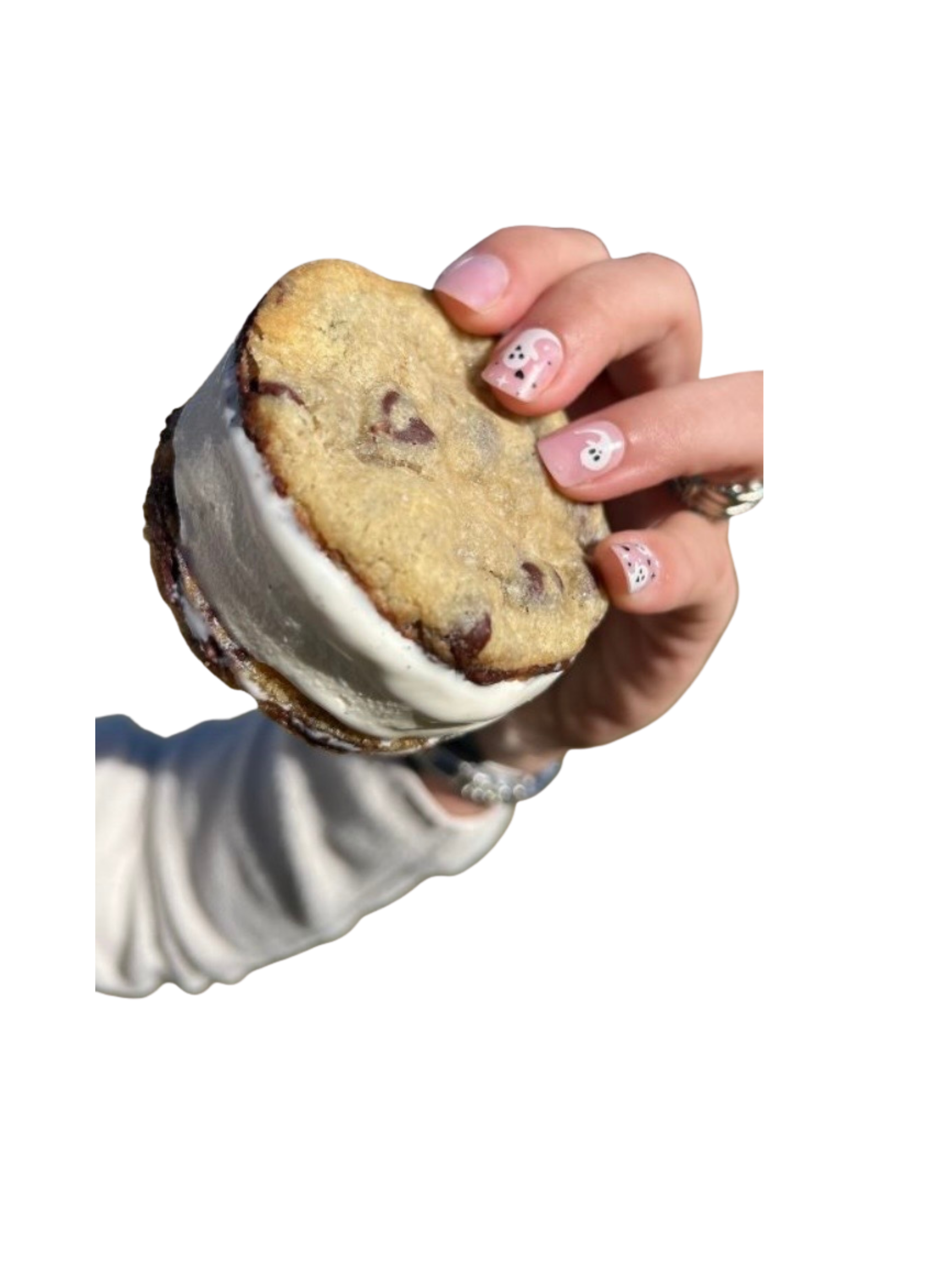 A hand with nails painted with playful ghost and pumpkin designs is holding a large chocolate chip cookie with ice cream in a bowl.