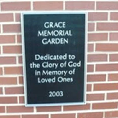 Black memorial plaque on brick wall with white text reading, 'Grace Memorial Garden Dedicated to the Glory of God in Memory of Loved Ones 2003'.