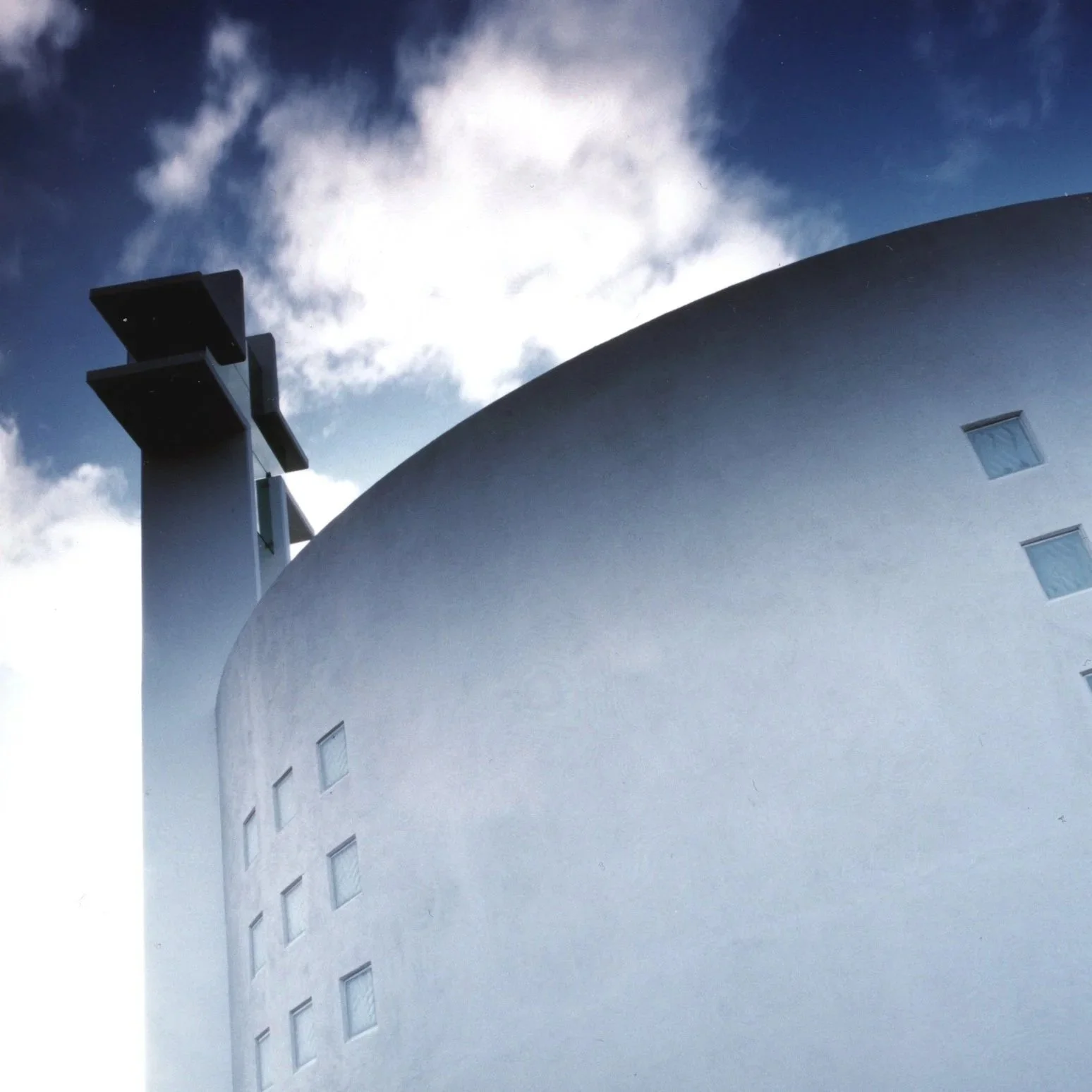 Close-up of a modern church building with rounded walls and small windows, under a partly cloudy sky.