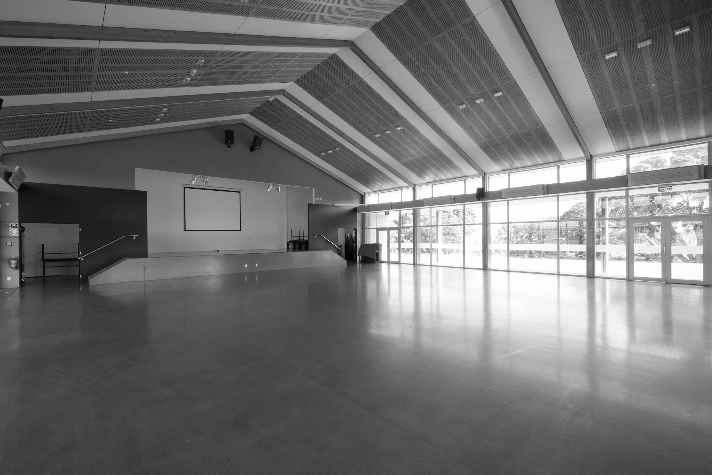A school hall, which can also be used for conferences or an event hall with large windows, high ceiling, and wooden flooring.