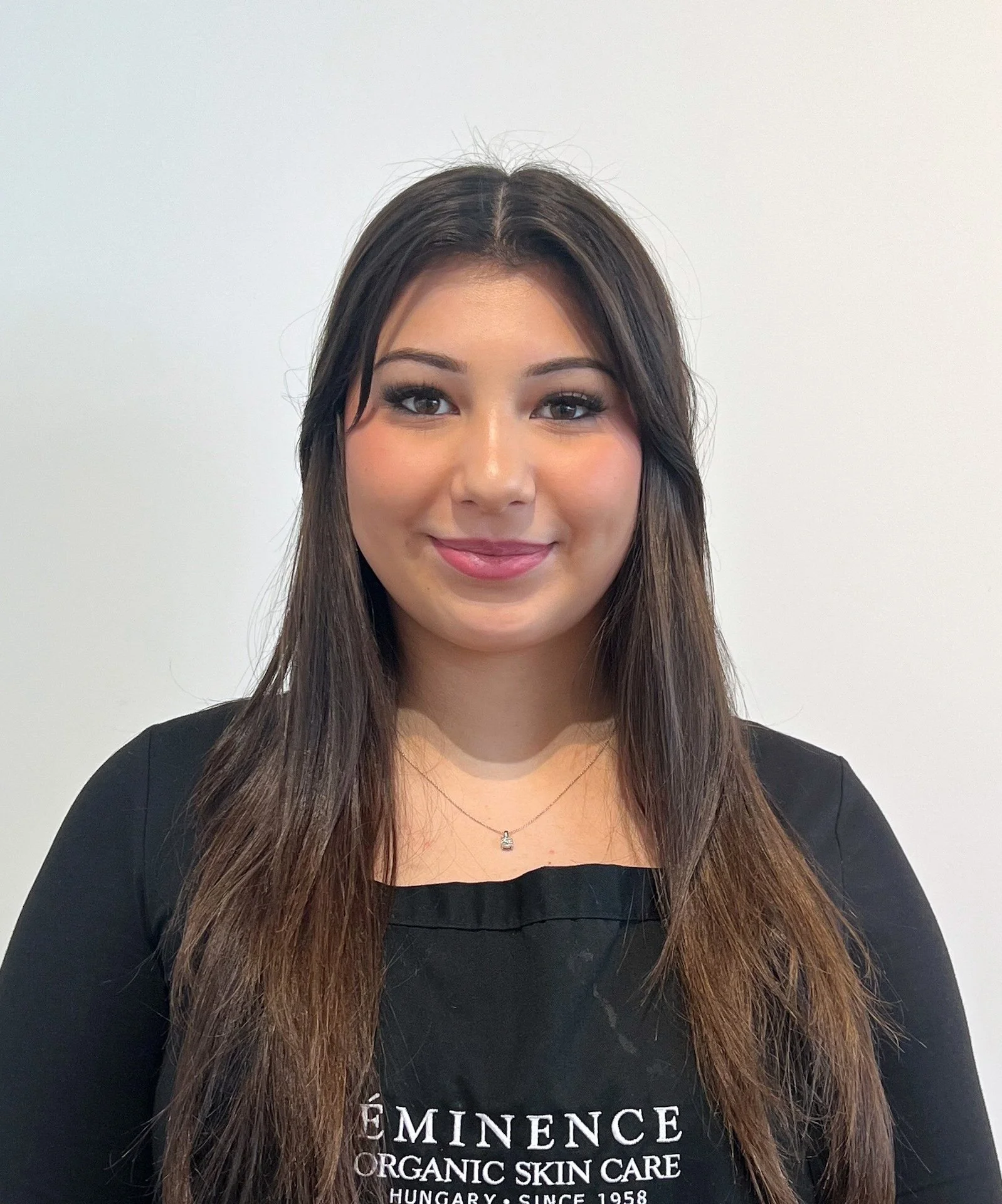 A young woman with long dark hair, wearing a black shirt with white text, standing against a plain white background.