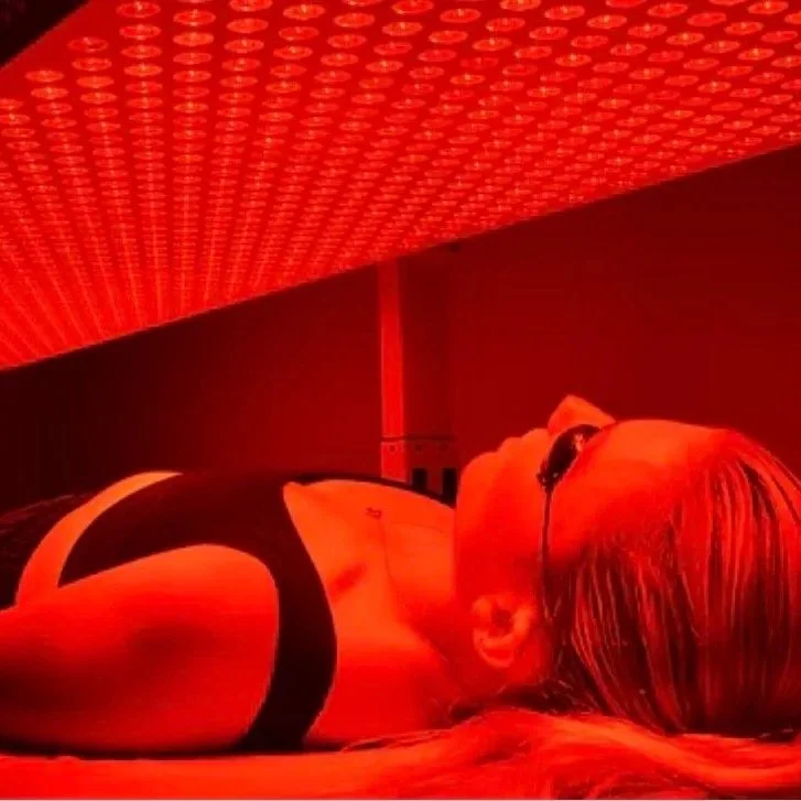 A woman lying down indoors under red lighting, wearing glasses and a black top.