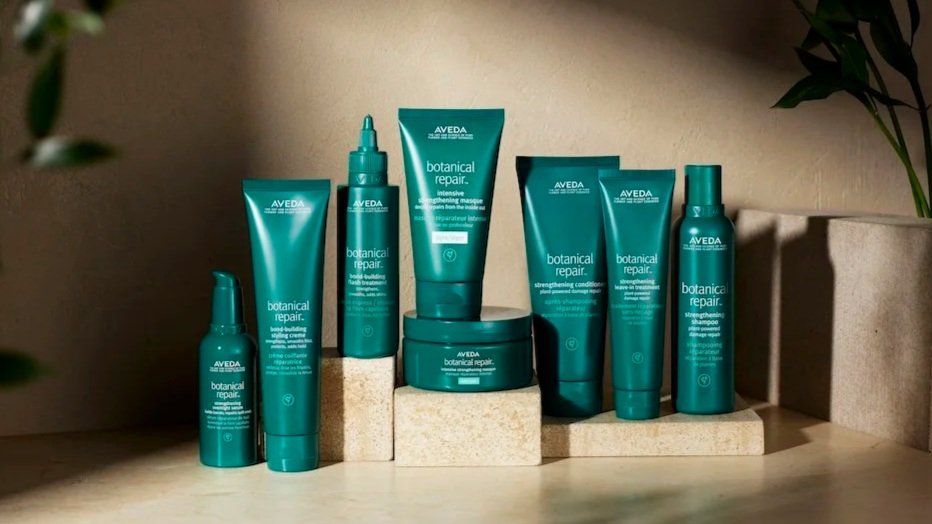 A collection of Aveda botanical repair hair care products arranged on beige blocks and a wooden surface.