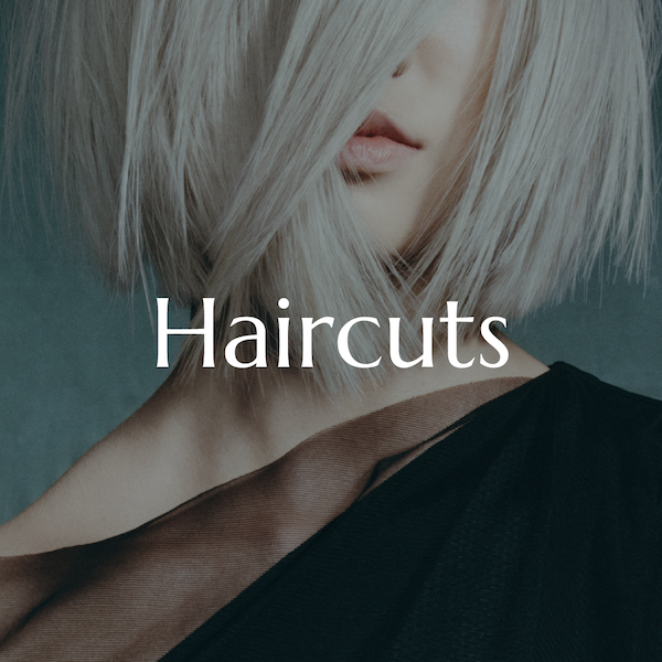 Close-up of a woman with platinum blonde, short, layered hair, wearing black clothing, with the word 'Haircuts' overlaid.