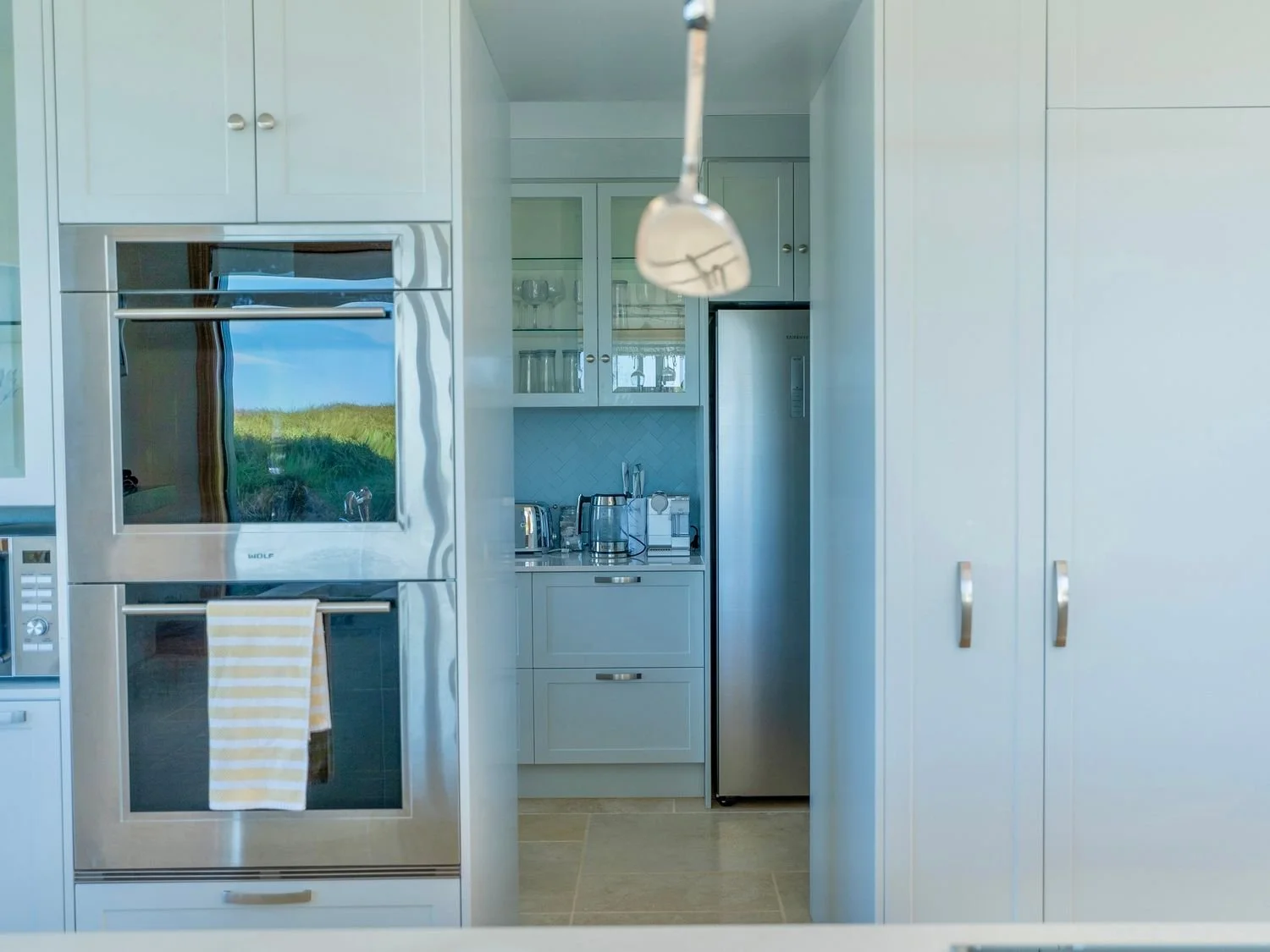 Kitchen with built-in oven, refrigerator, and cabinets, with a view of outdoor landscape reflected in the oven window at Opito Point Lodge, luxury beachfront accommodation.