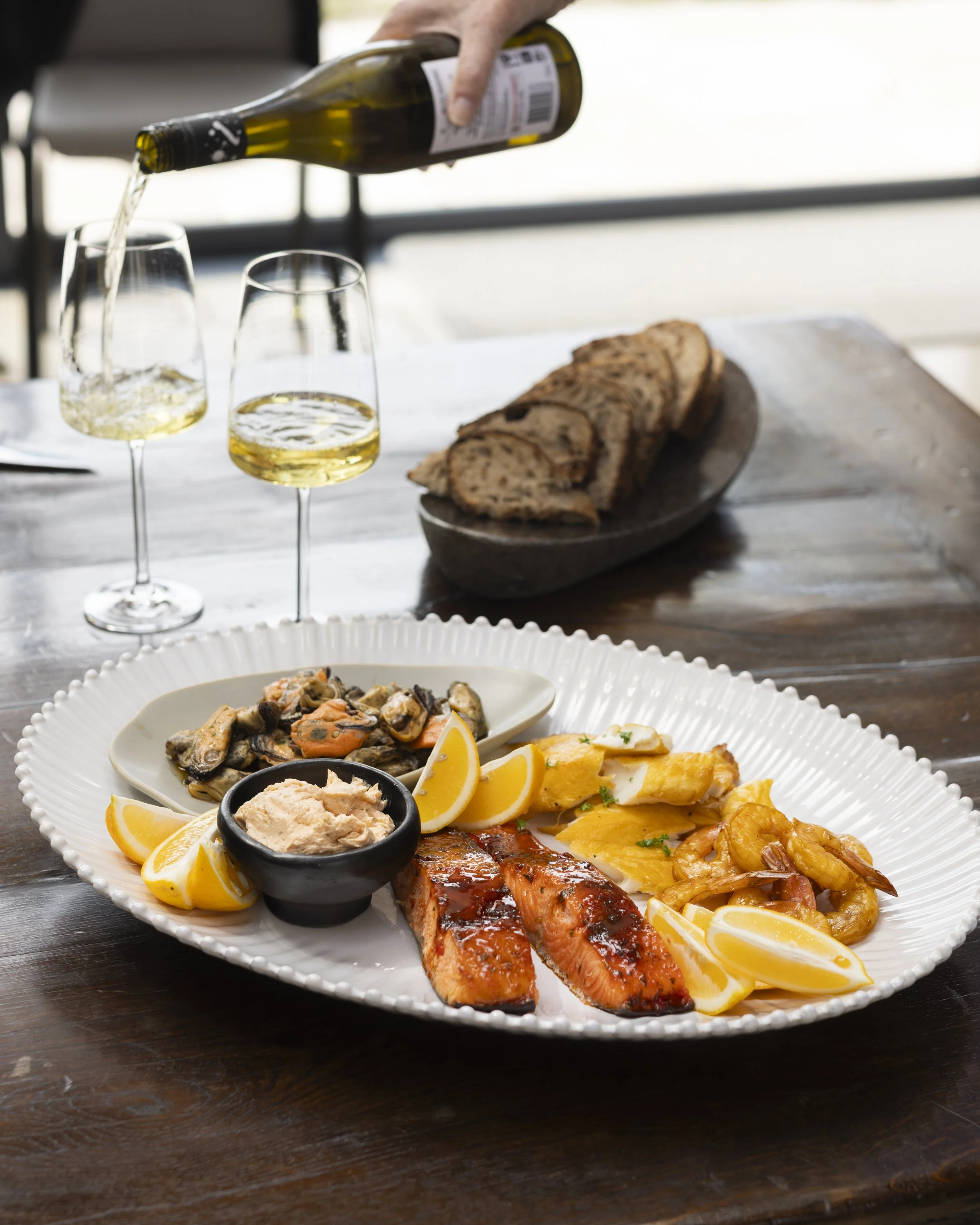 A dining table with a plate of cooked salmon, lemon wedges, shrimp, vegetables, a small bowl of dip, and a side dish of mushrooms and carrots. Fine Dining at Opito Point Lodge - Luxury Accommodation in Coromandel, New Zealand