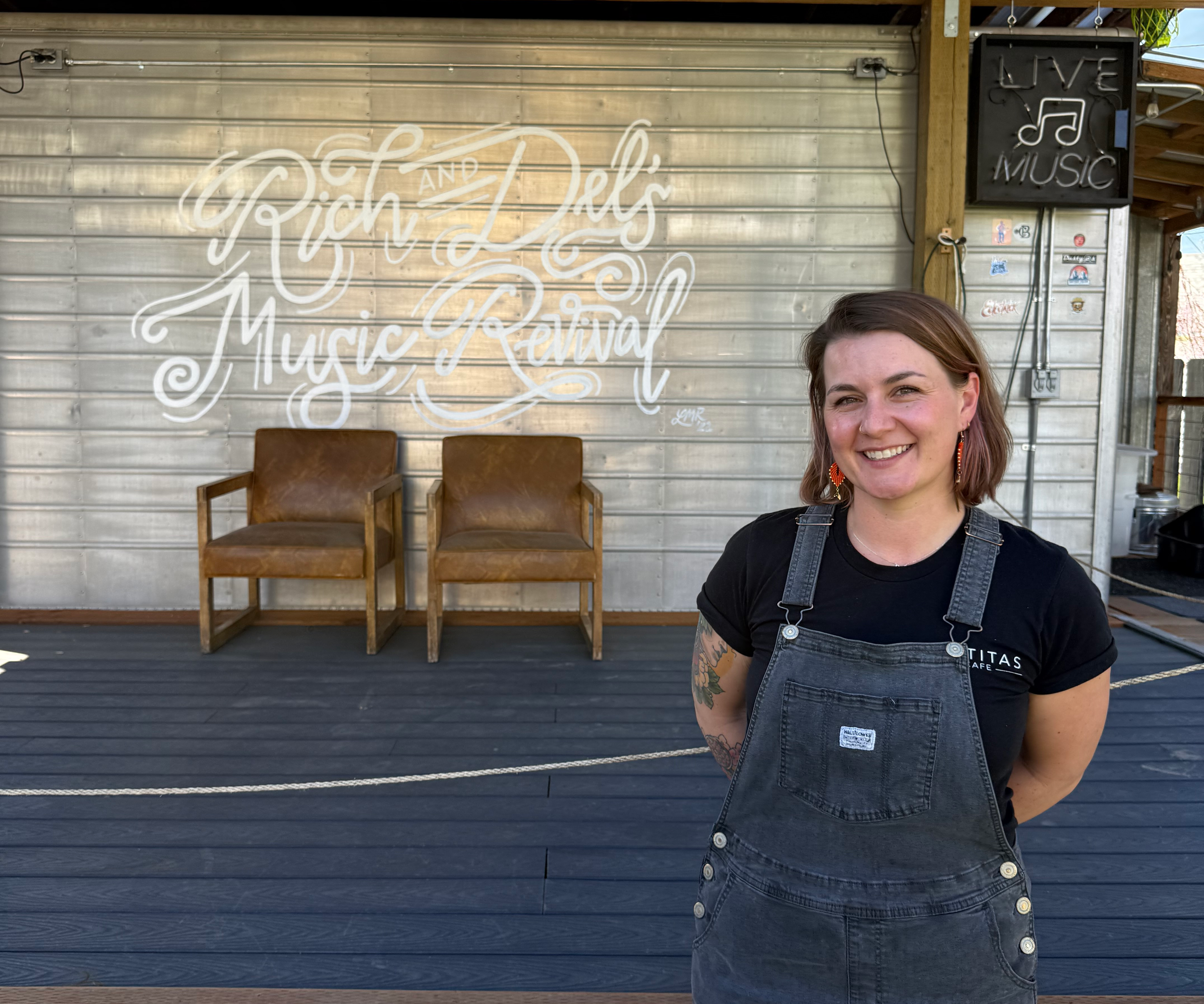 A young woman standing in front of an outdoor stage with a sign that reads "Rich and Del's Music Revival"