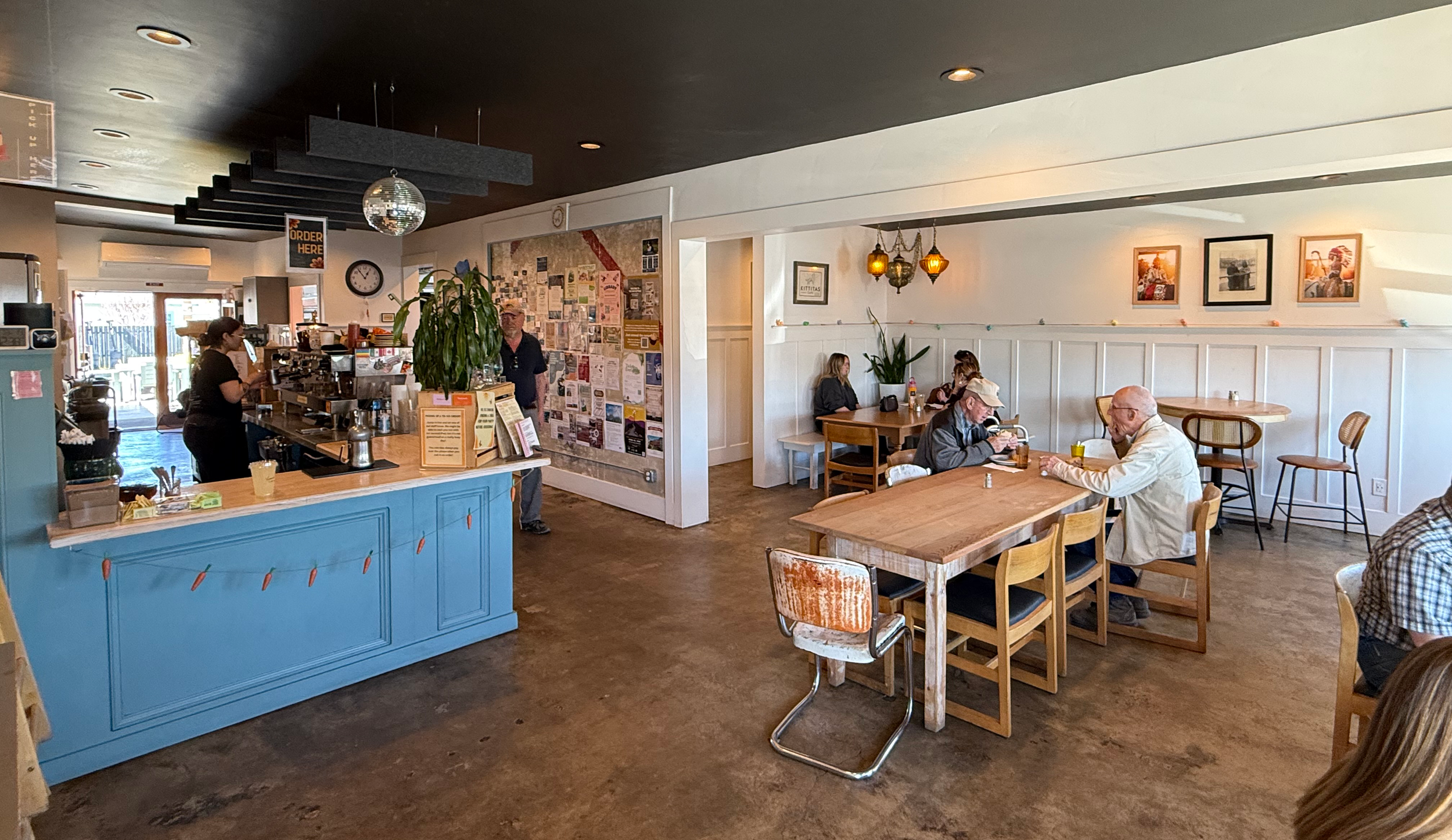 Customers enjoying lunch at a long wooden Kittitas Café and a barista making espresso drinks at the coffee bar.