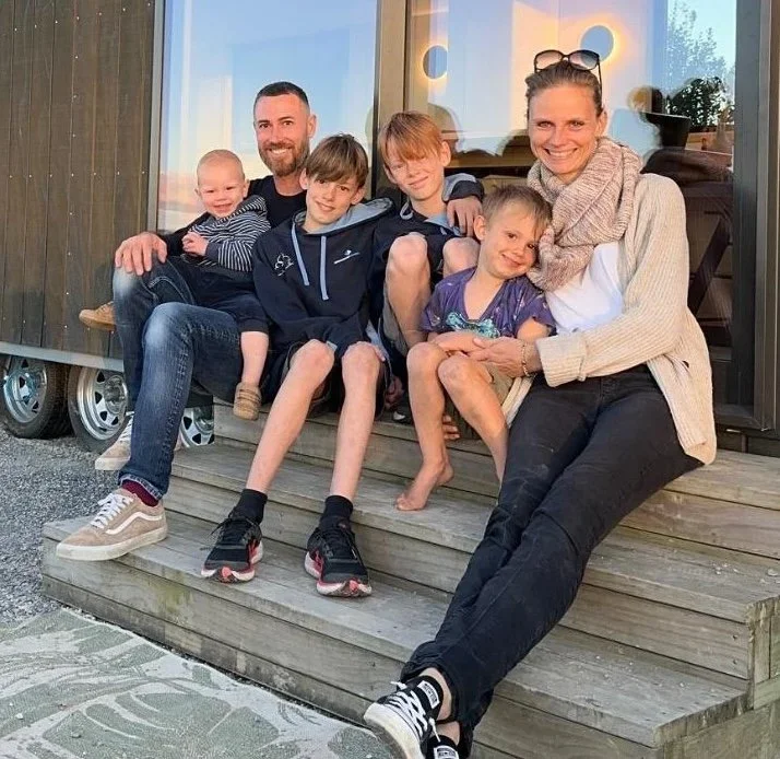 Family sitting together on wooden steps outside their home, smiling and enjoying each other's company.