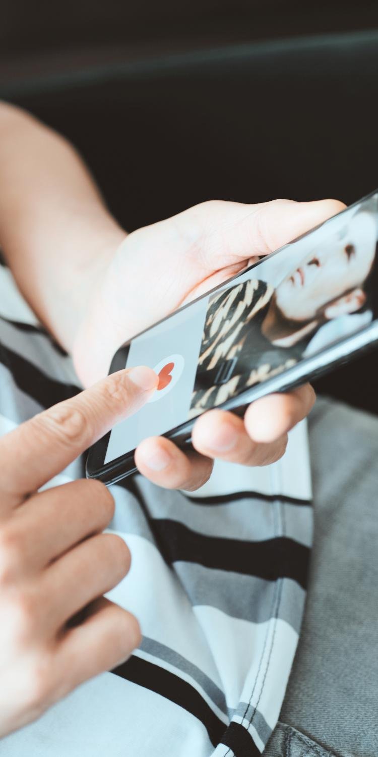 A person holding a smartphone and using a dating app, with a blurred close-up photo of a woman on the screen.