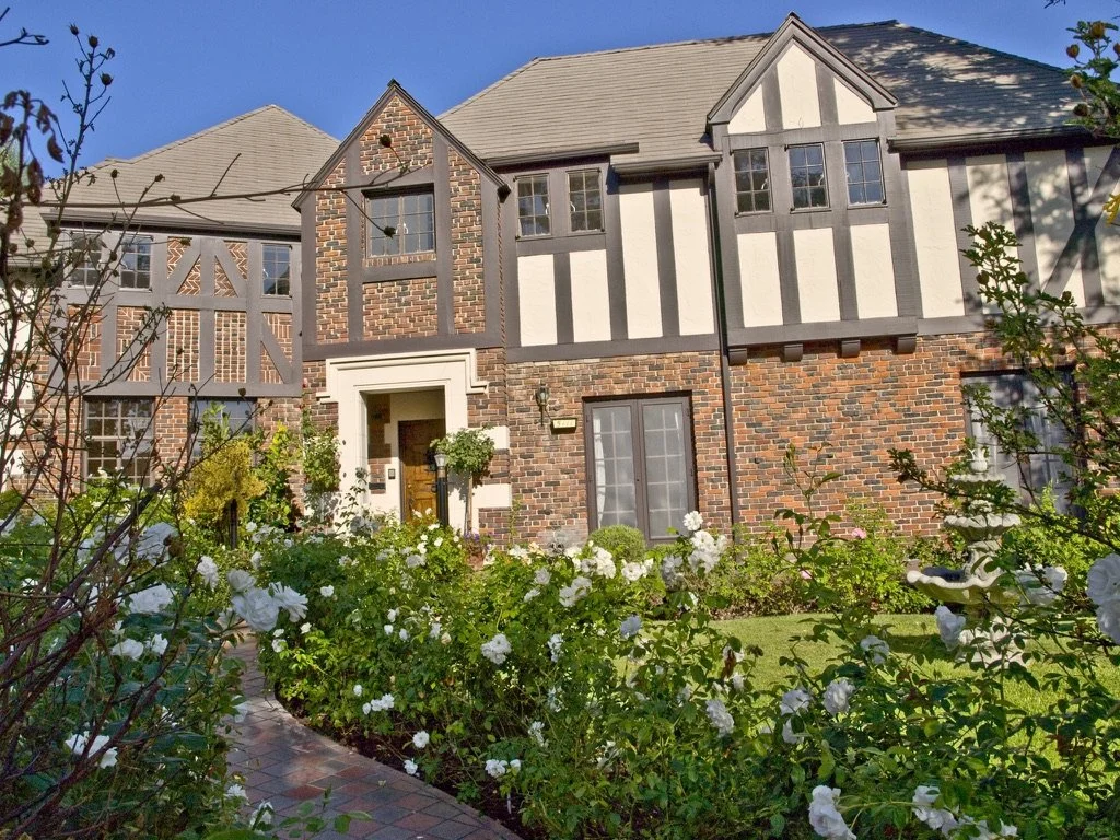 Presented by Missig Team, a real estate team at Berkshire Hathaway HomeServices California Properties in Beverly Hills and Los Angeles. Front view of a two-story Tudor house in Los Feliz with a brick and half-timbered exterior, surrounded by a garden
