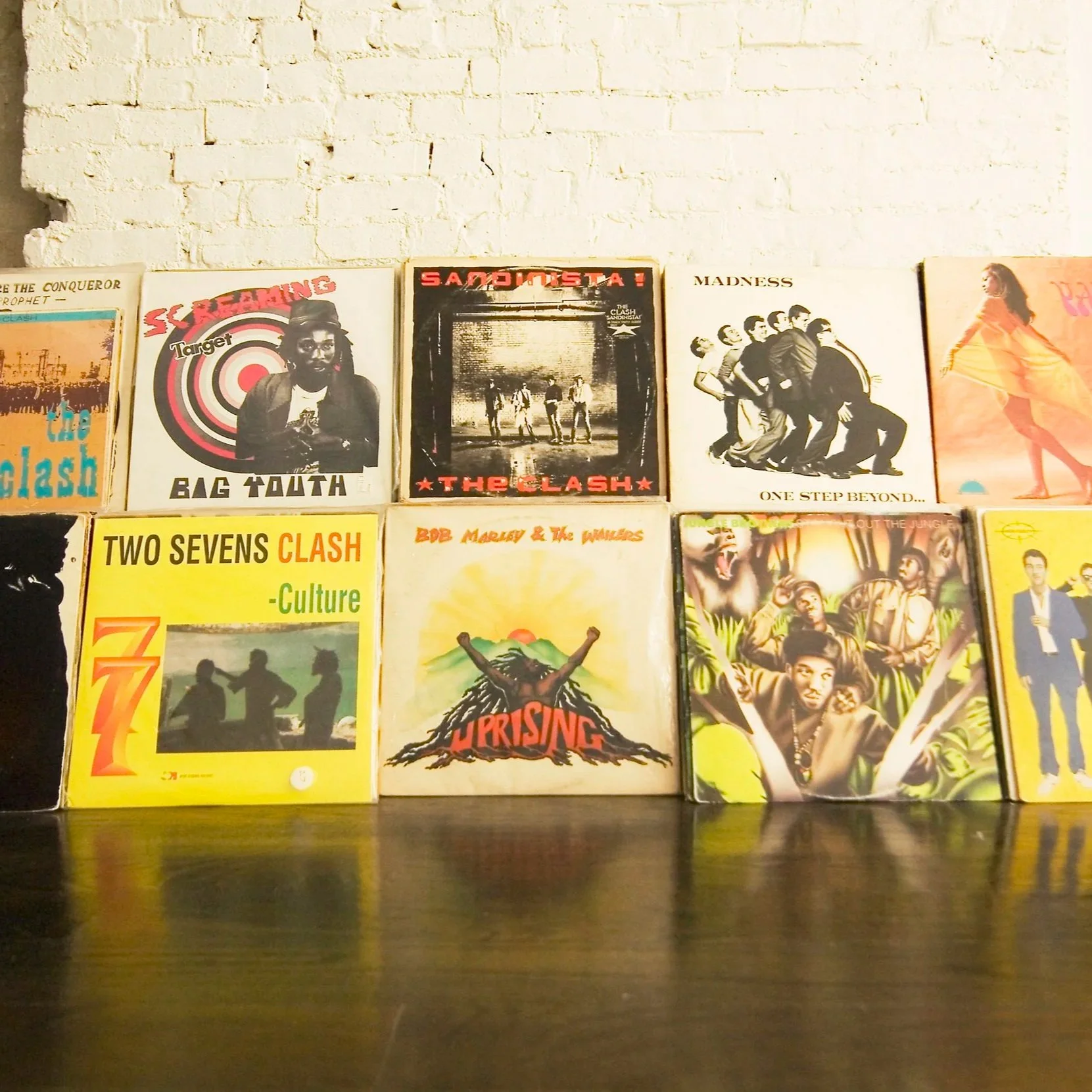 A collection of vintage vinyl record covers arranged in two rows against a white brick wall background.