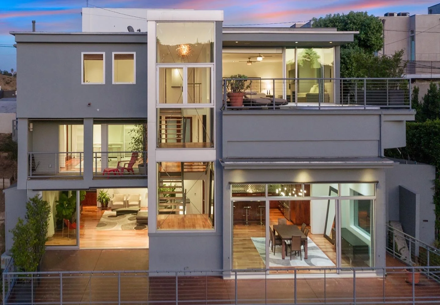 Presented by Missig Team, a real estate team at Berkshire Hathaway HomeServices California Properties in Beverly Hills and Los Angeles. Modern multi-story house in Sunset Plaza with large glass windows and a large balcony, illuminated interior, at su