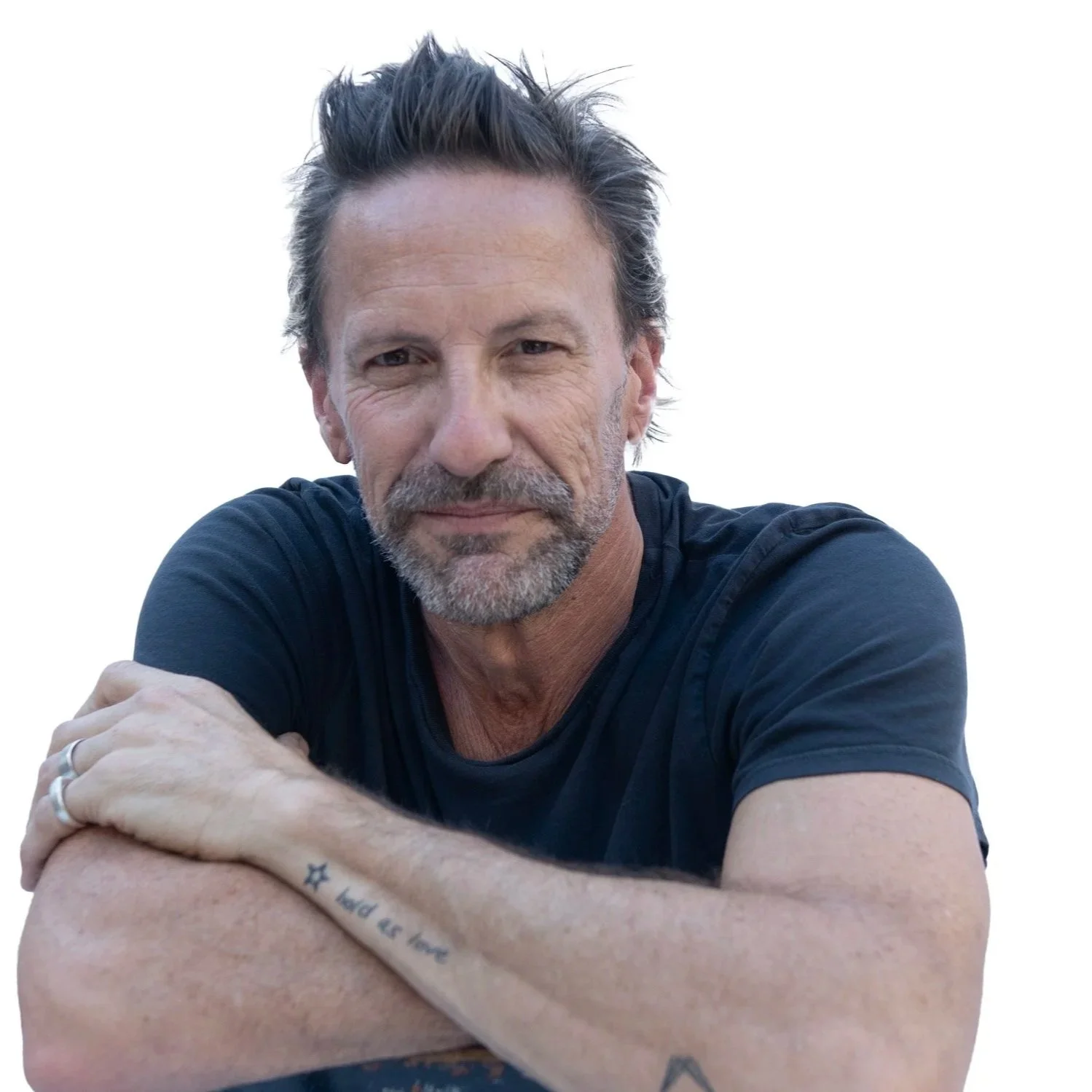 Jeff Forney, wearing a black t-shirt, is resting his arms on a surface with a white background.