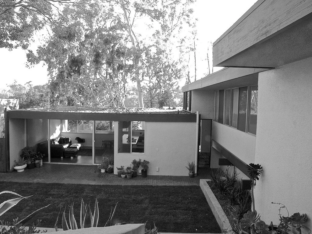 Presented by Missig Team, a real estate team at Berkshire Hathaway HomeServices California Properties in Beverly Hills and Los Angeles. A black and white photo of a Mid-Century Modern post and beam house in Silver Lake with large windows and a garden