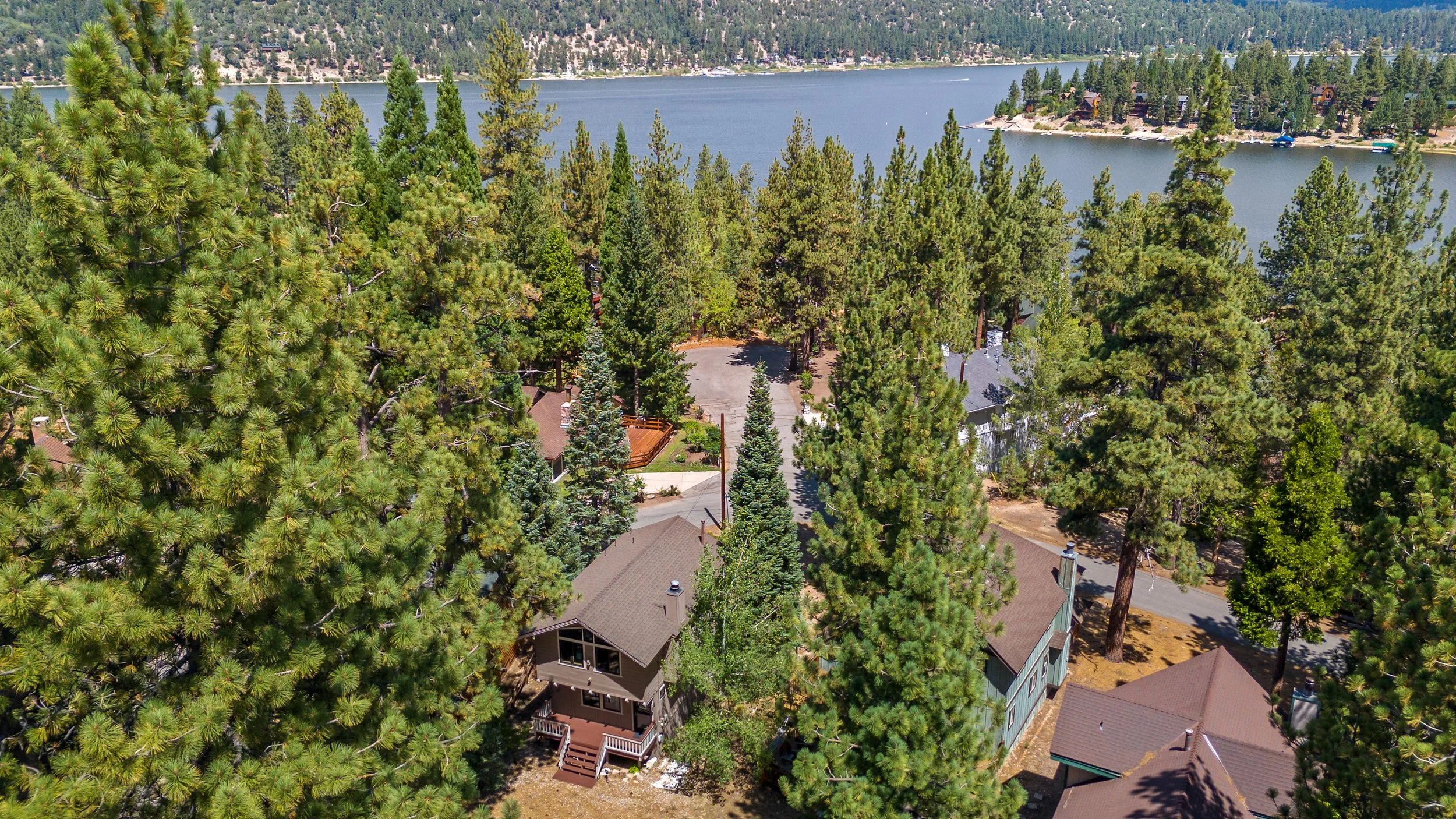 Presented by Missig Team, a real estate team at Berkshire Hathaway HomeServices California Properties in Beverly Hills and Los Angeles. A Big Bear cabin amongst the trees with Big Bear Lake in the background.