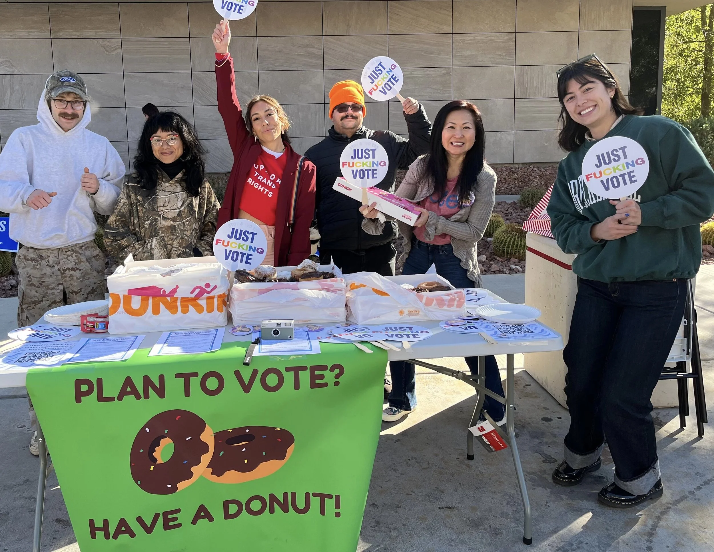 Volunteers with Just Fucking Vote signs at Donuts and Democracy table.