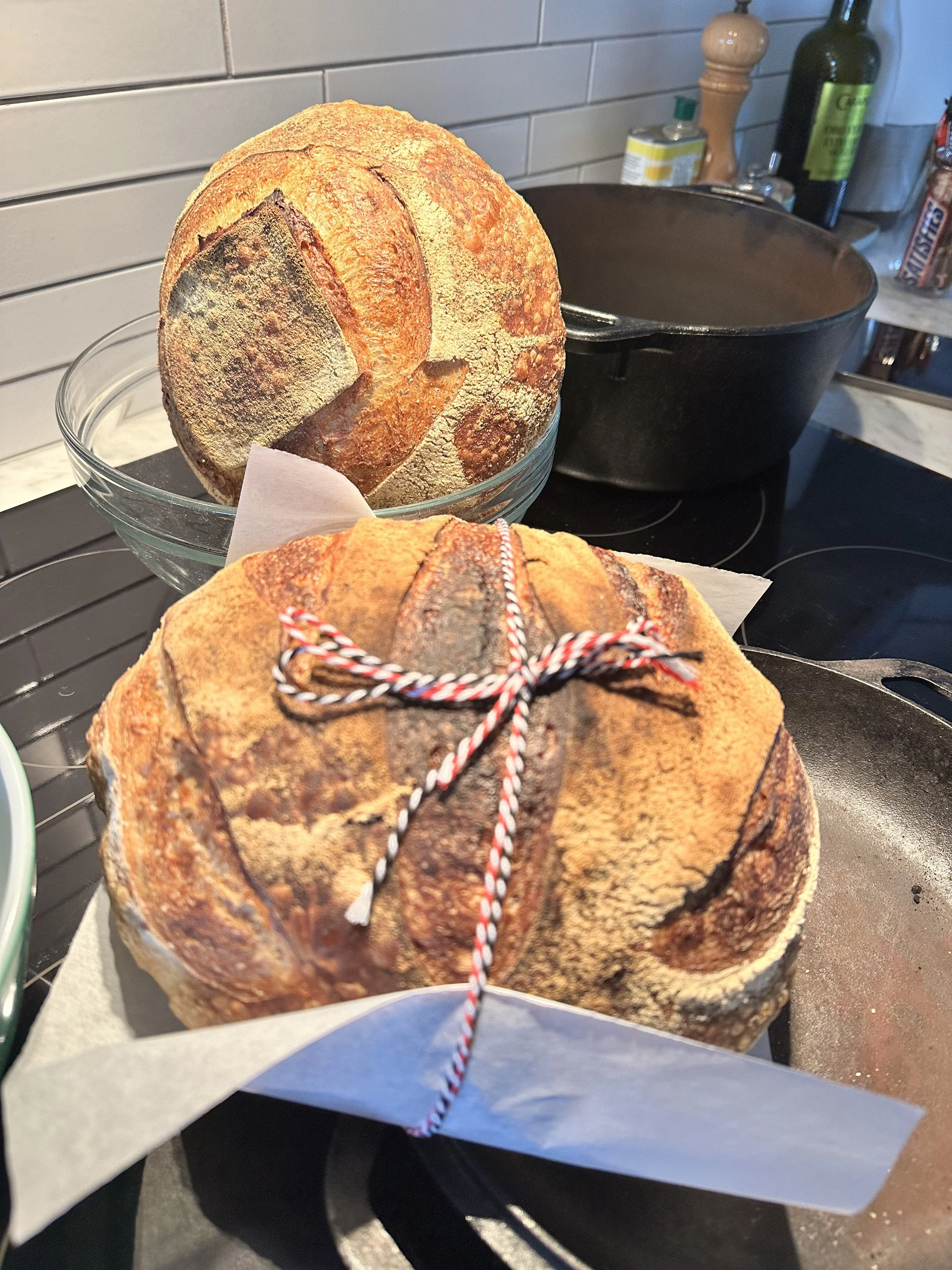 Two loaves of freshly baked round sourdough bread on a kitchen counter, one topped with a string tied in a bow.