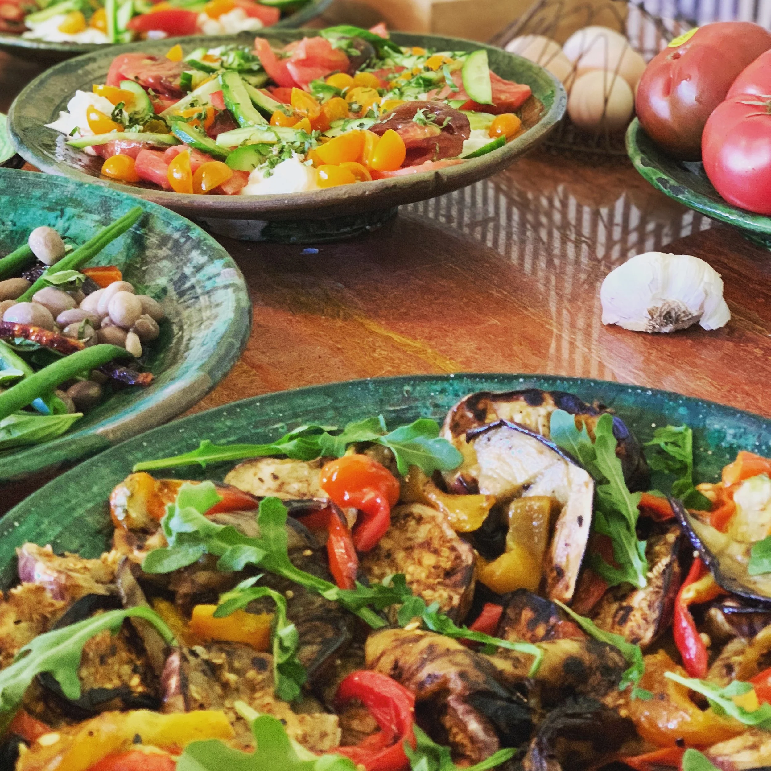 Assorted salads and roasted vegetables on green plates on a wooden table.