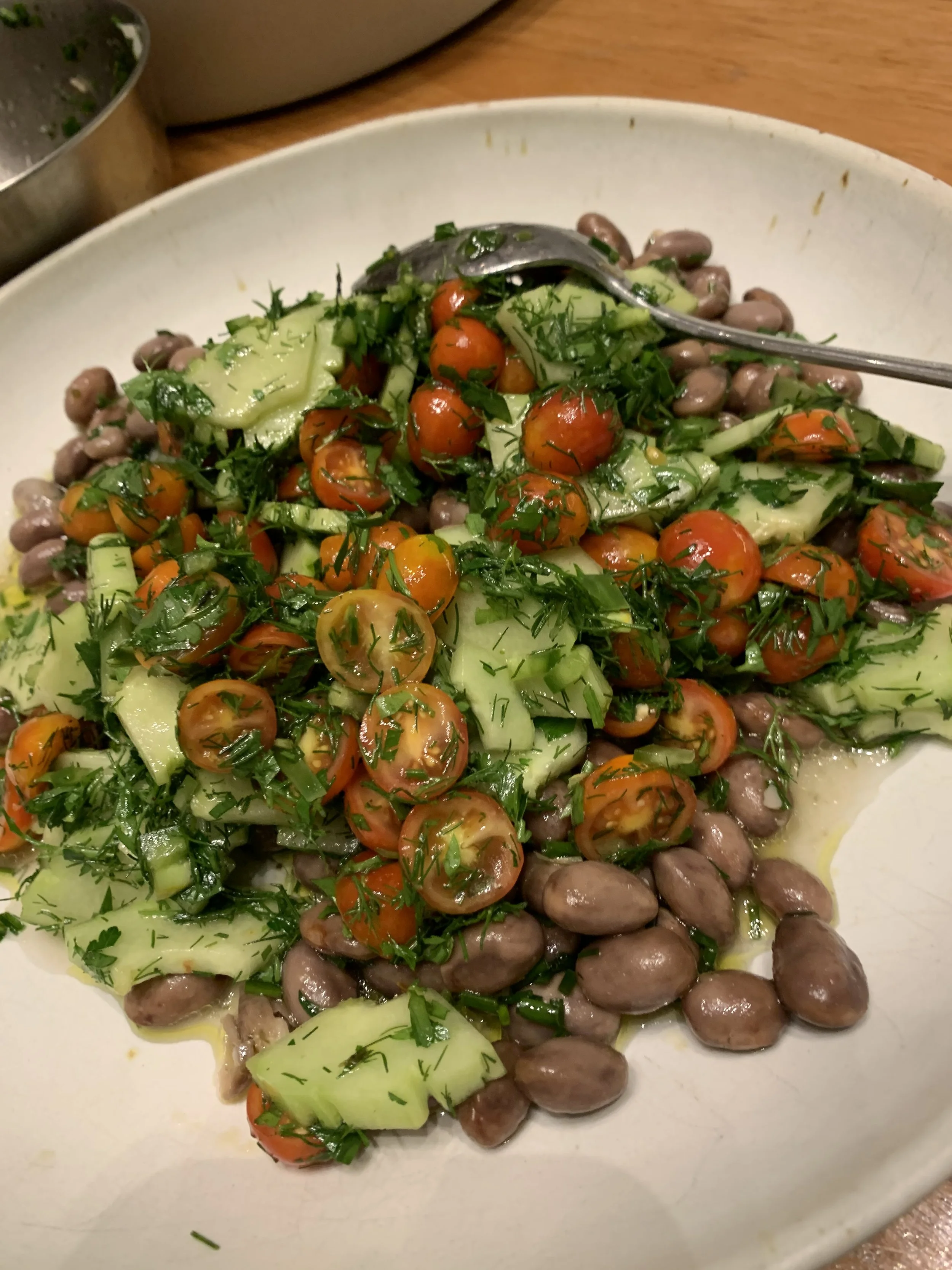 A plate of mixed bean salad with cherry tomatoes, chopped cucumbers, garnished with fresh herbs.