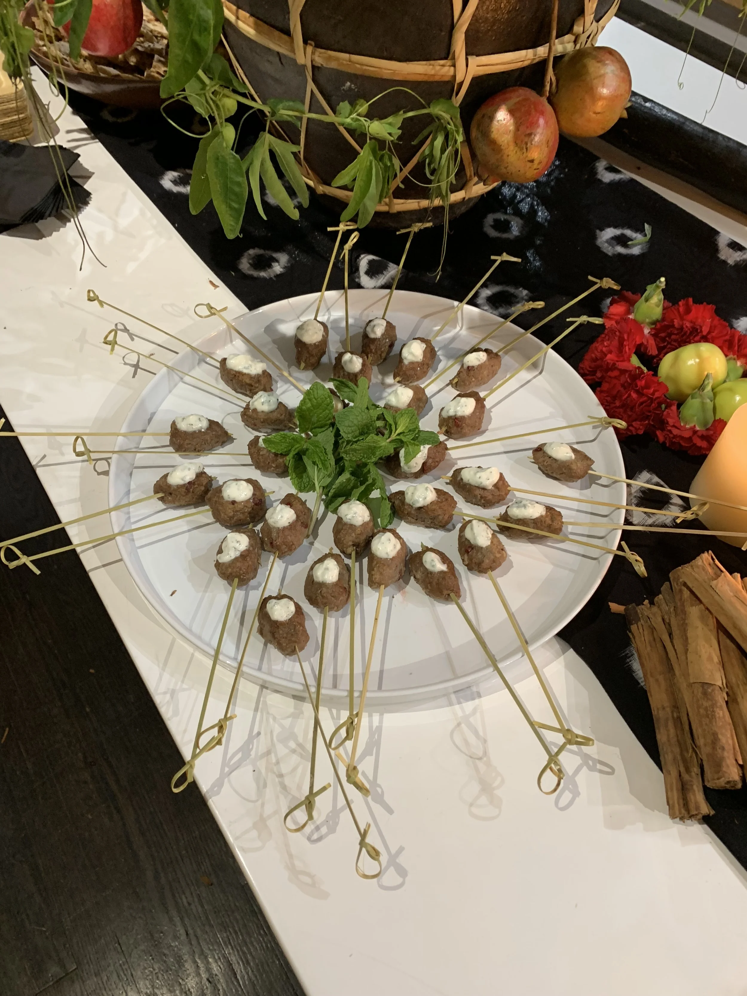 Plate of skewered appetizer or meatballs garnished with fresh mint, served on a white tray at a party or gathering.