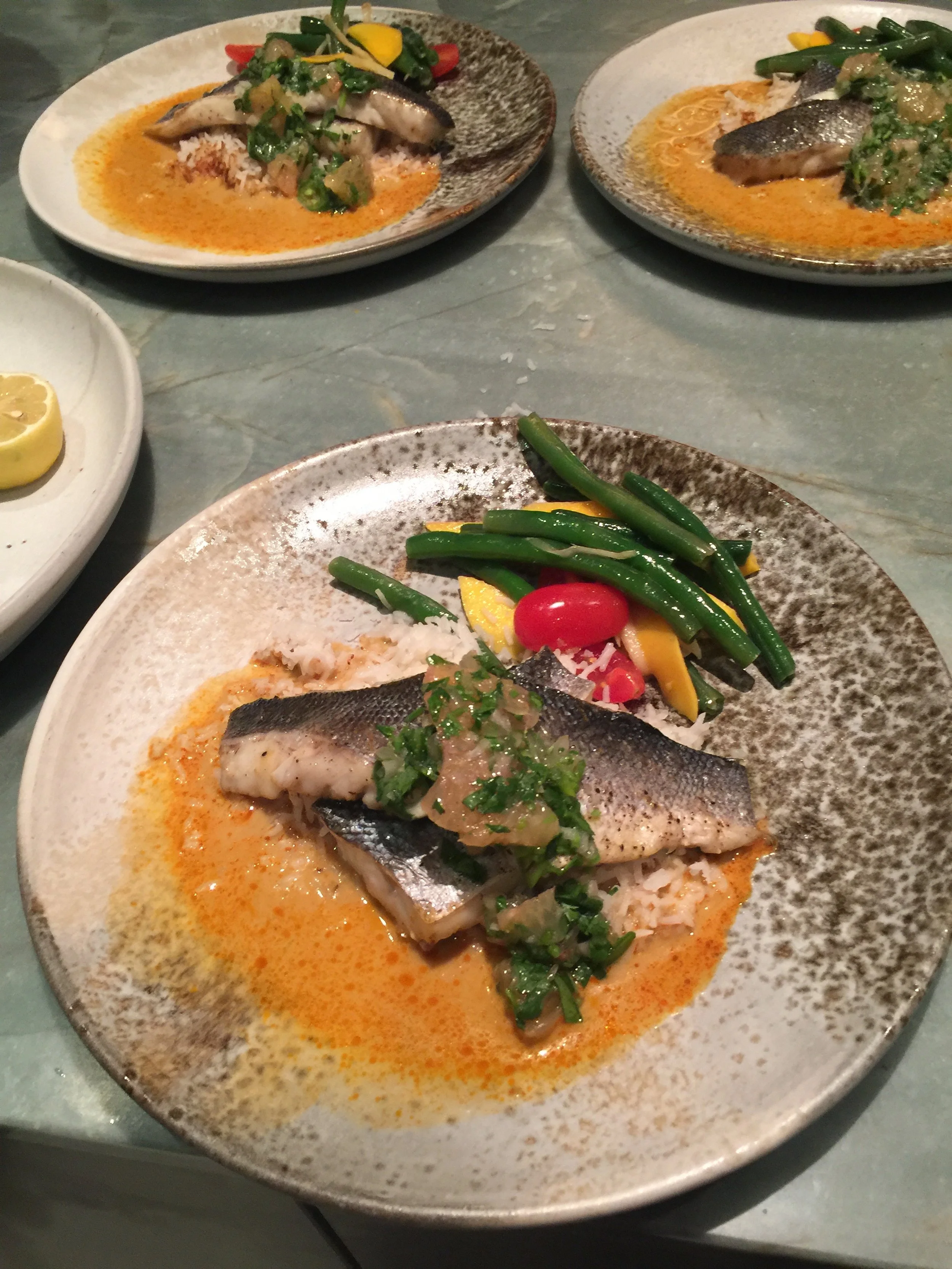 Plate of cooked fish topped with green herbs, served with a side of green beans and cherry tomatoes.