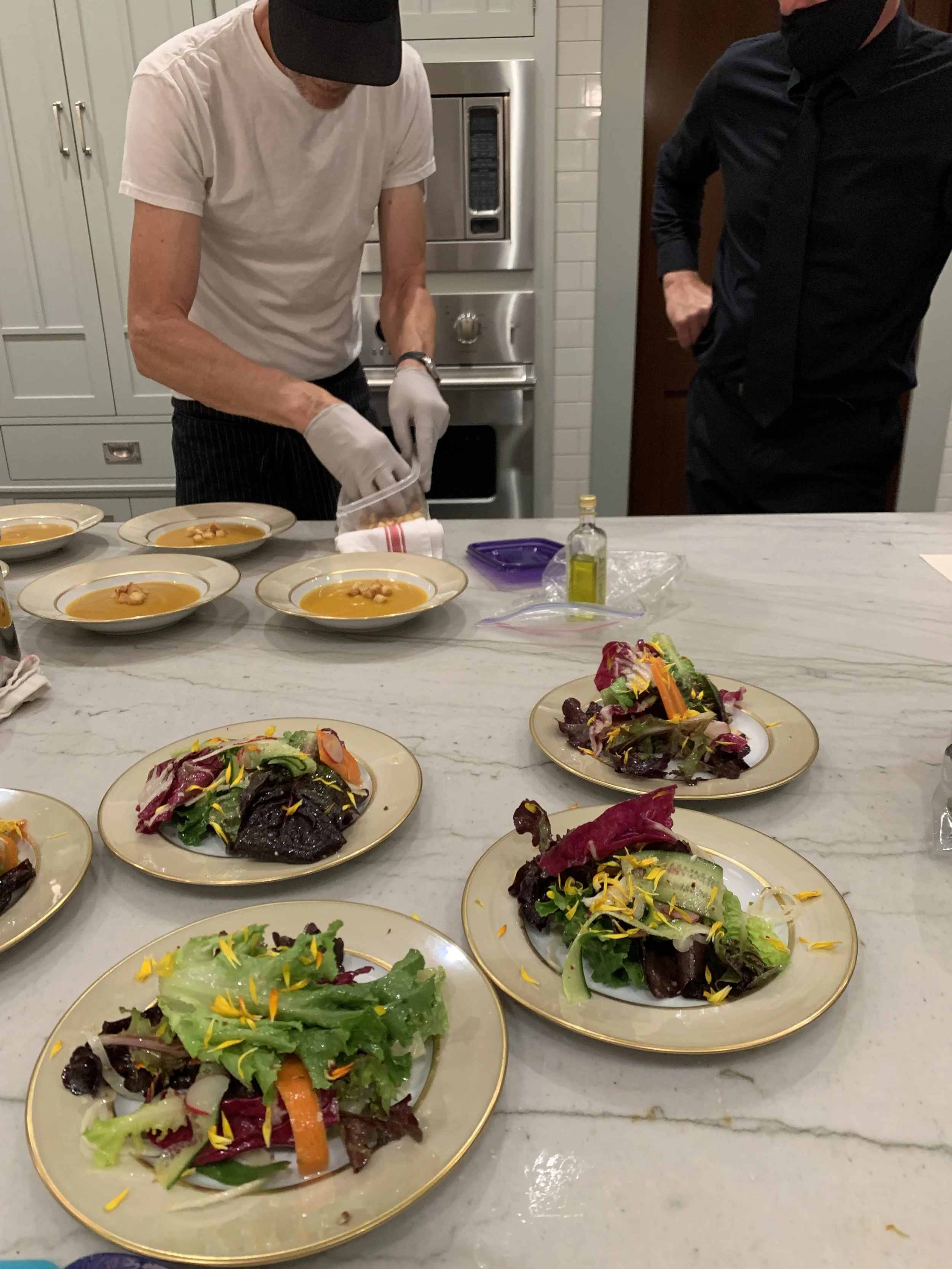 Chef preparing soup in a kitchen with salads on plates on the table.