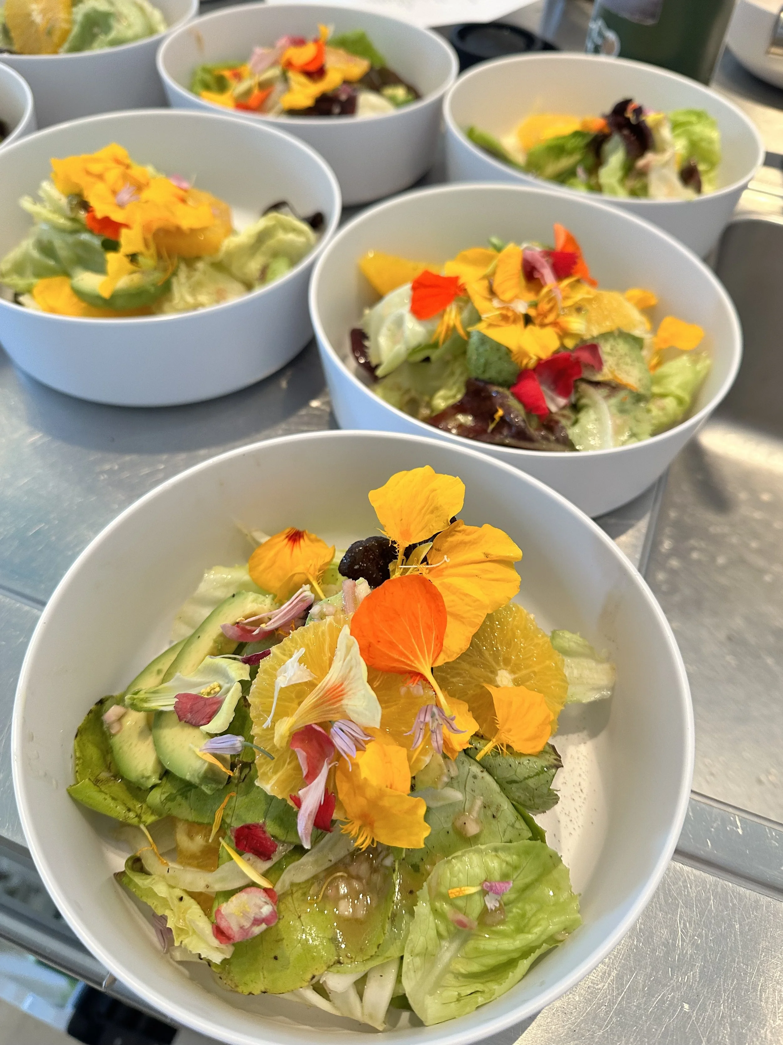 Bowl of mixed greens salad garnished with edible flower petals and slices of citrus fruit