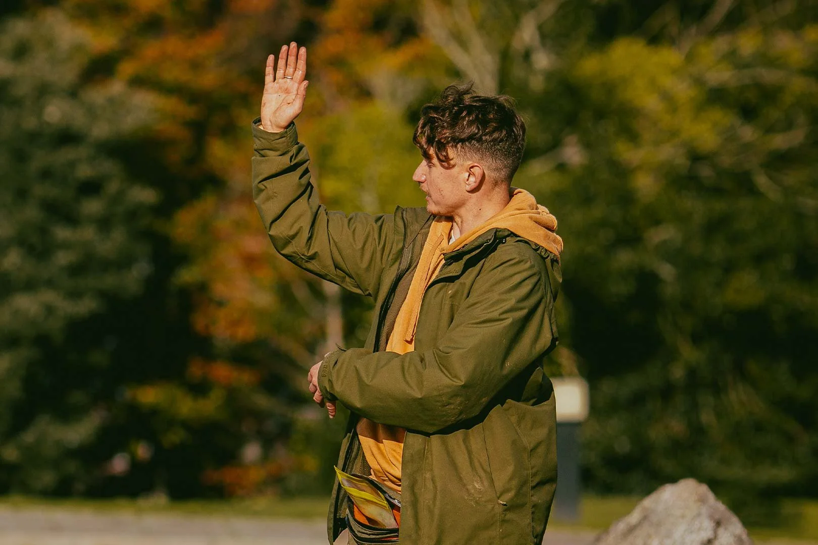 Young man in outdoor park raising his right hand in an urban setting with fall foliage.