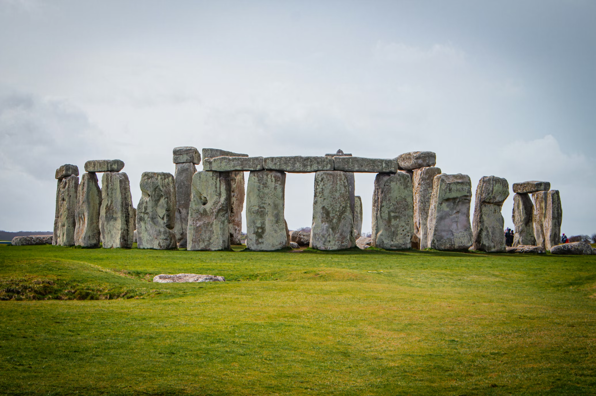 Photo of Stonehenge, a prehistoric monument in England, with large standing stones arranged in a circular formation on green grass under a cloudy sky.