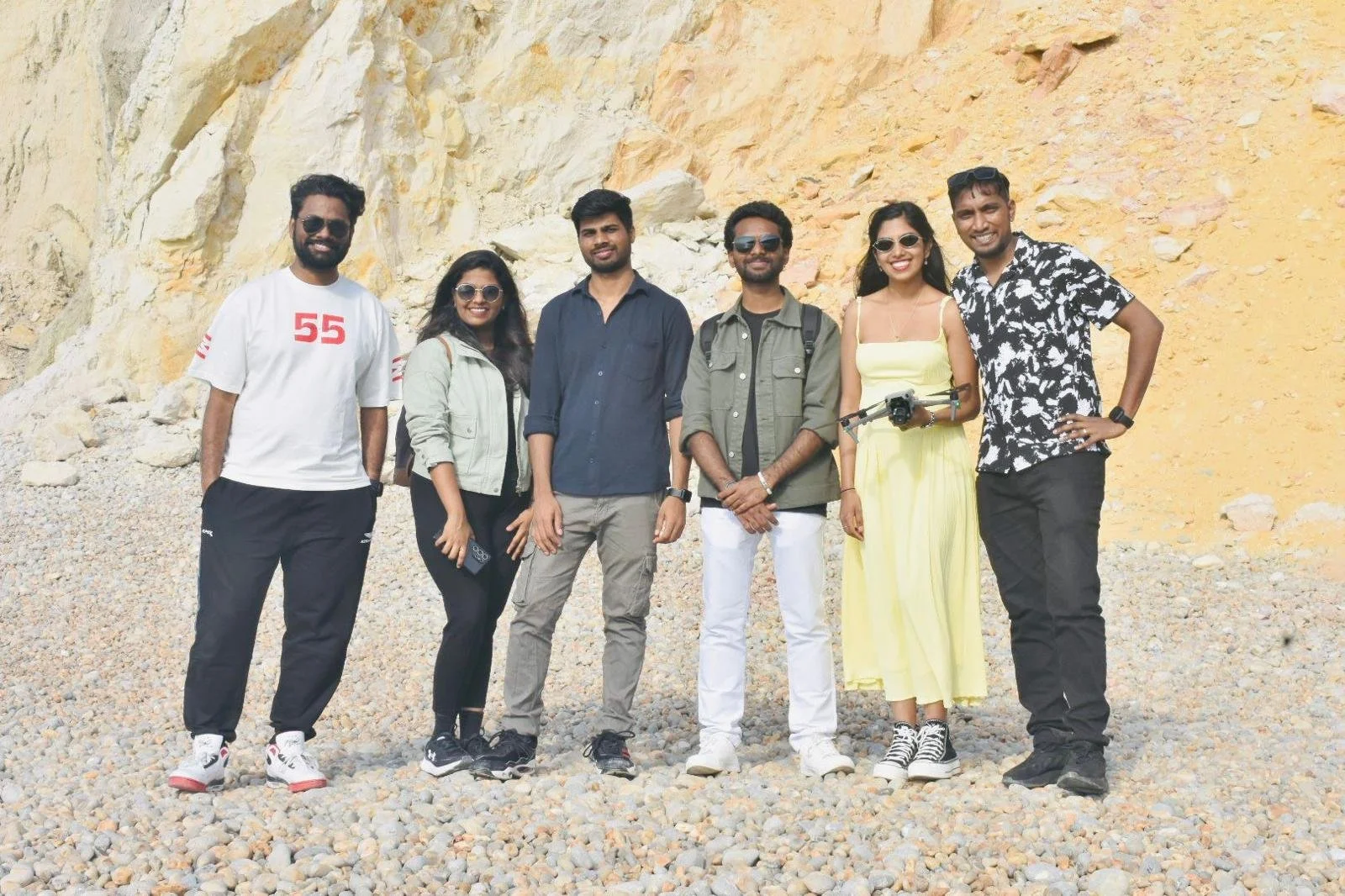 Group of seven people standing on rocky beach with yellow cliff behind them.