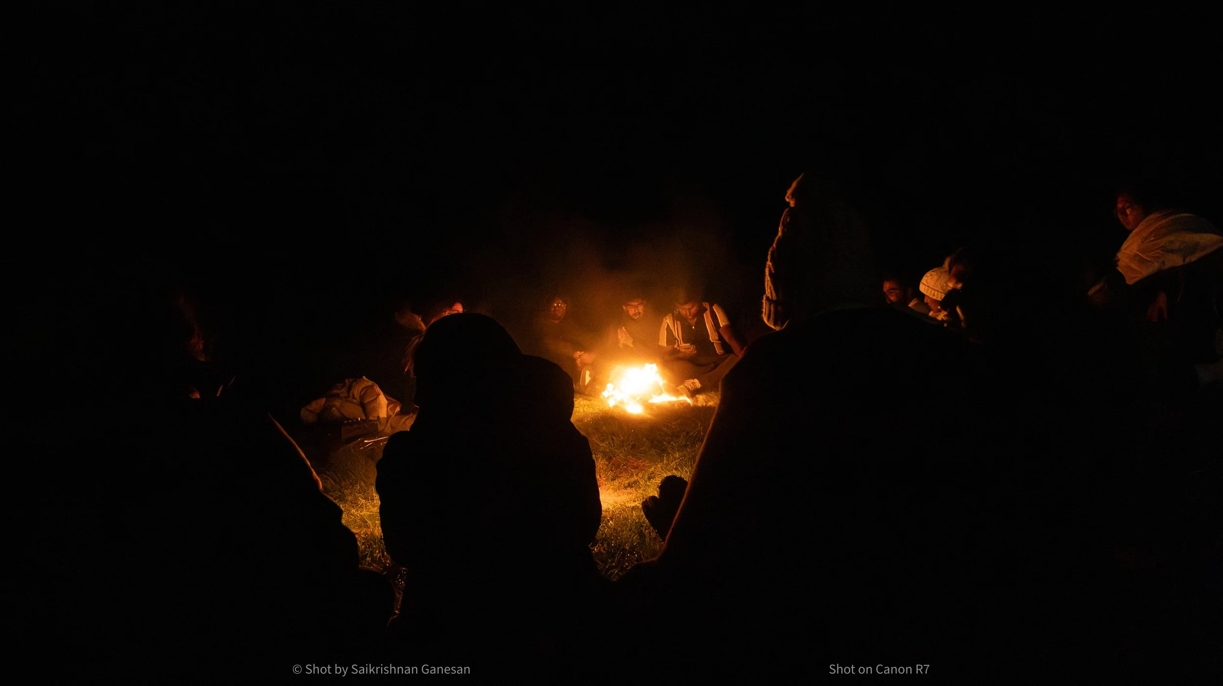 A group of people sitting around a campfire at night in a circular formation.