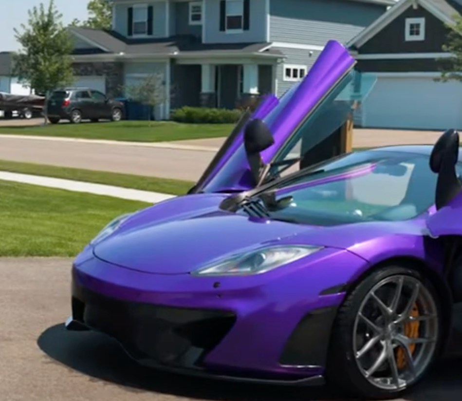 A purple sports car with its gullwing door open, parked in front of a house.