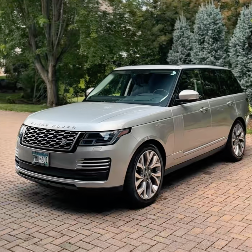 Silver Range Rover SUV parked on brick driveway with trees and greenery in the background.