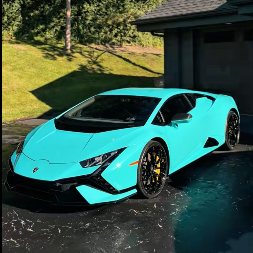 A bright blue Lamborghini Huracán parked in a driveway with a garage, next to a grassy area with trees.