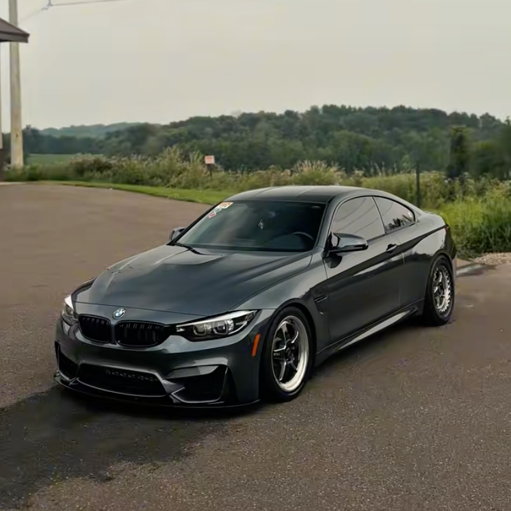 Black BMW coupe parked on a paved surface with greenery and hills in the background.