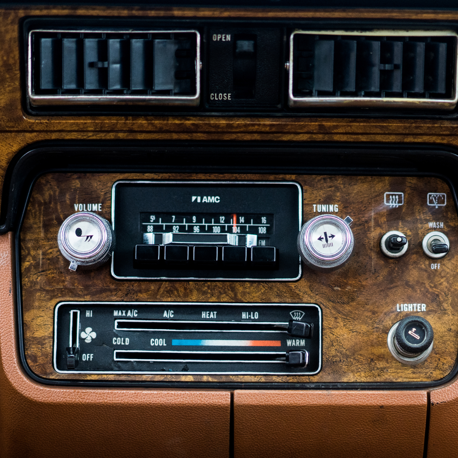 View of a vintage car dashboard featuring wood paneling, an AM radio, and controls for heating, cooling, and other functions.