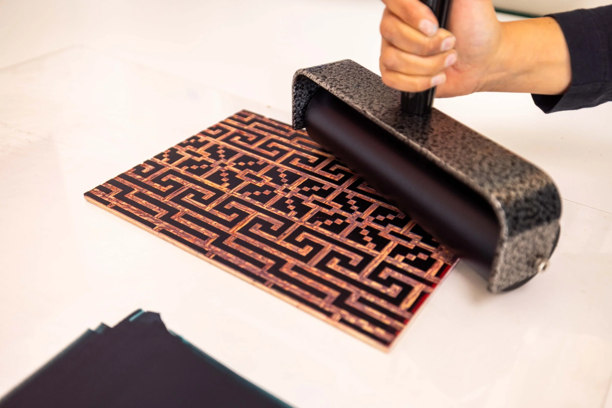 A person is pressing down a roller on a linocut with a maze-like pattern.